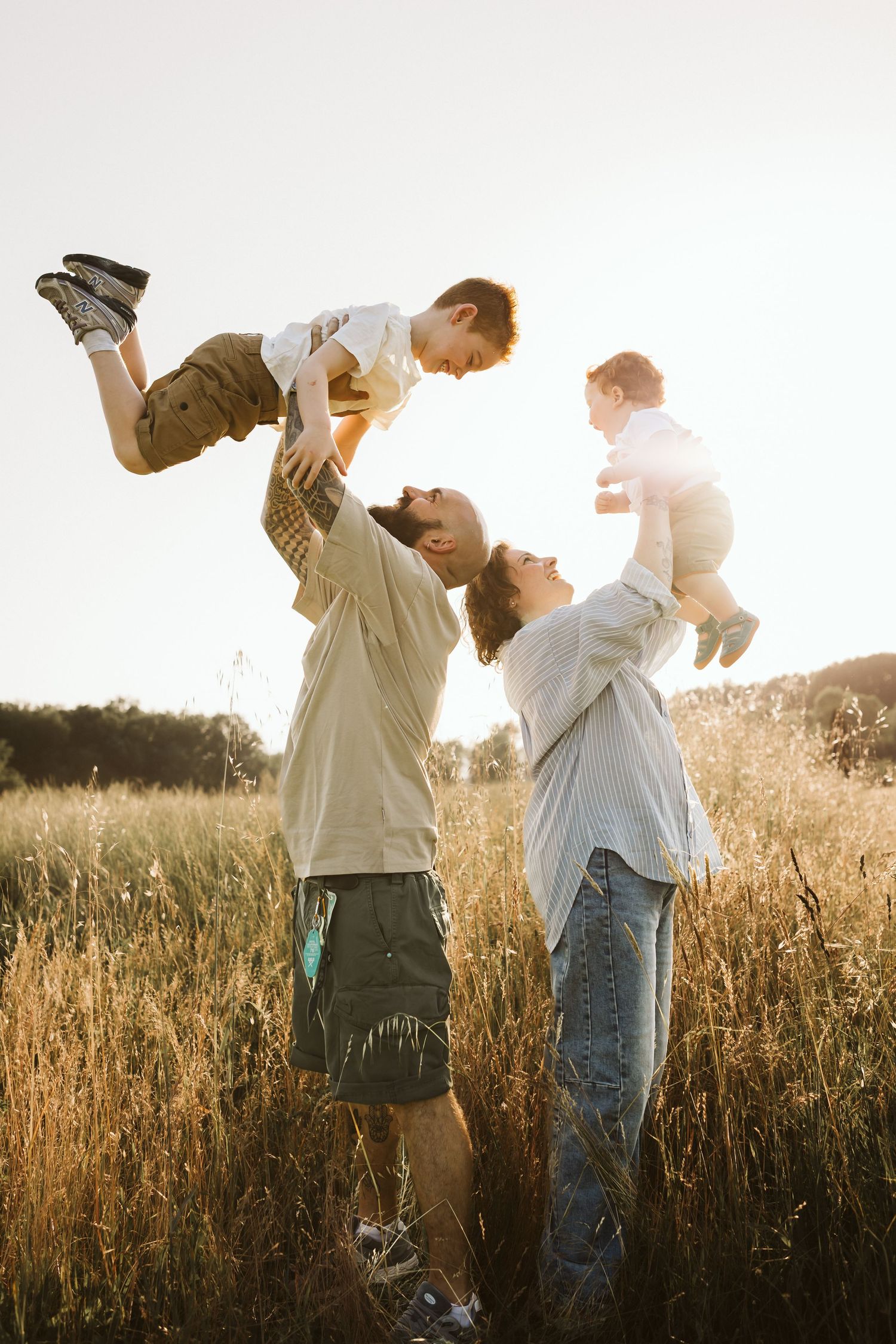 Parents lifting two young children in golden field at sunset.