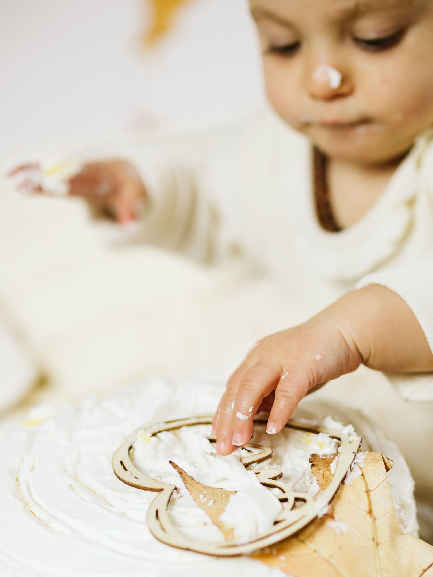 Baby in white outfit smashing birthday cake with hands covered in frosting.