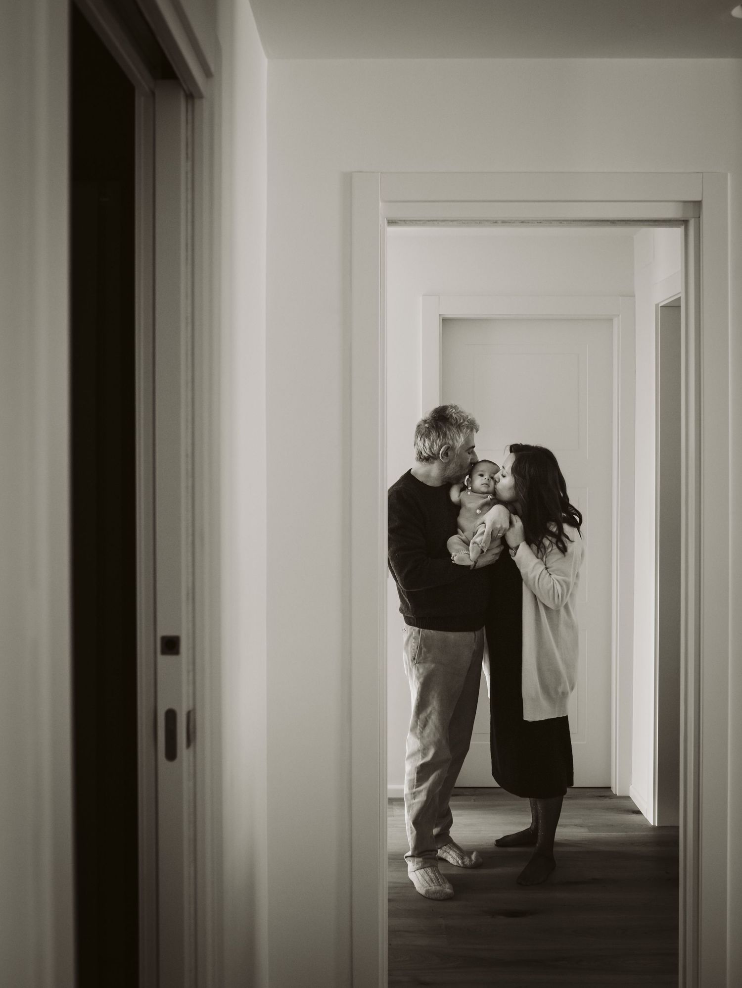 Black and white photo of couple sharing a tender moment with newborn in a hallway.
