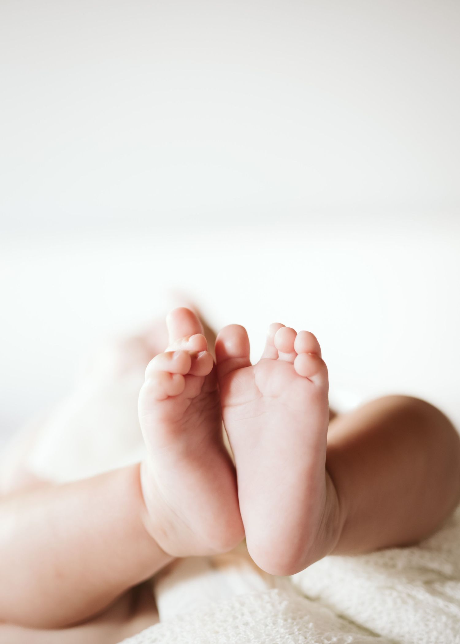 Close-up of tiny newborn baby feet resting on a soft white blanket.
