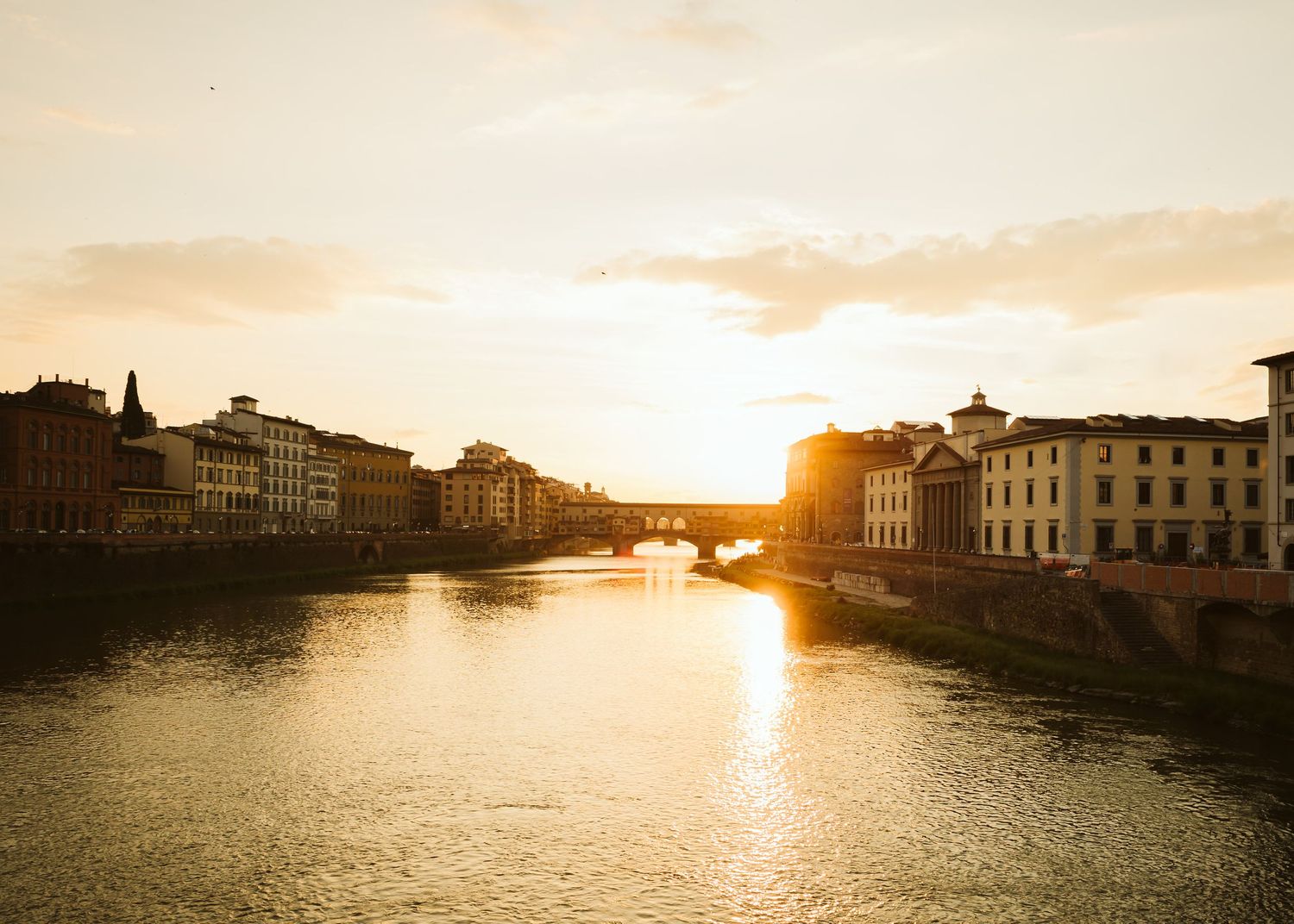 Golden sunset reflecting on the Arno River with Ponte Vecchio bridge in Florence, Italy.
