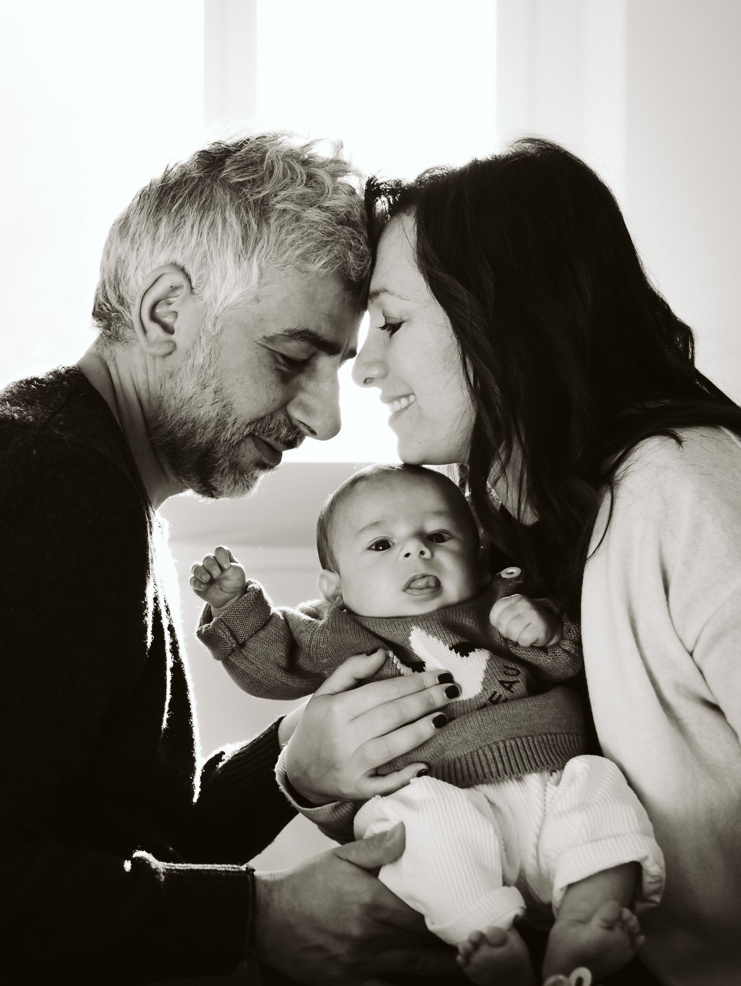 Black and white portrait of parents touching foreheads while holding newborn baby.