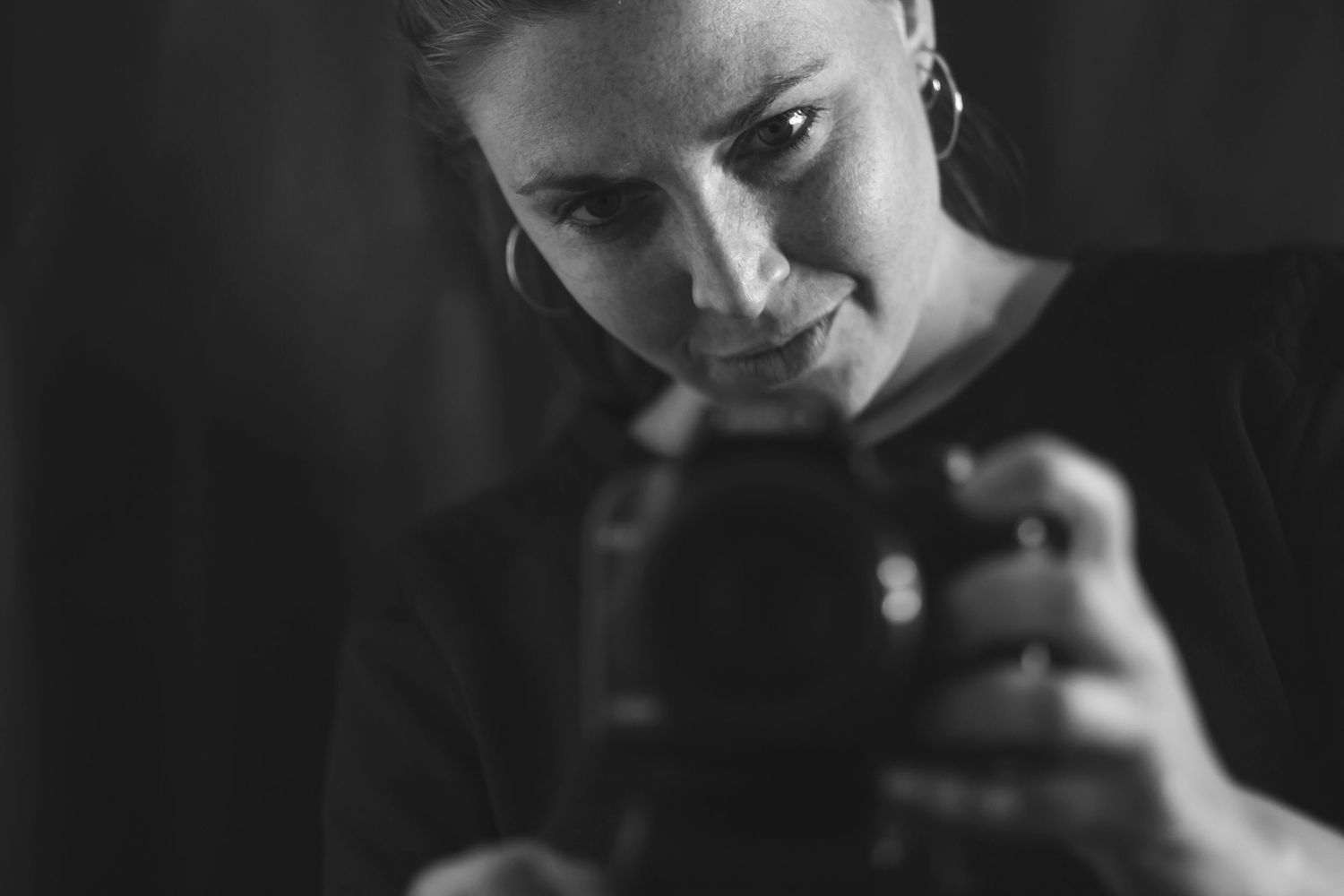 Black and white portrait of female photographer holding camera in low light.