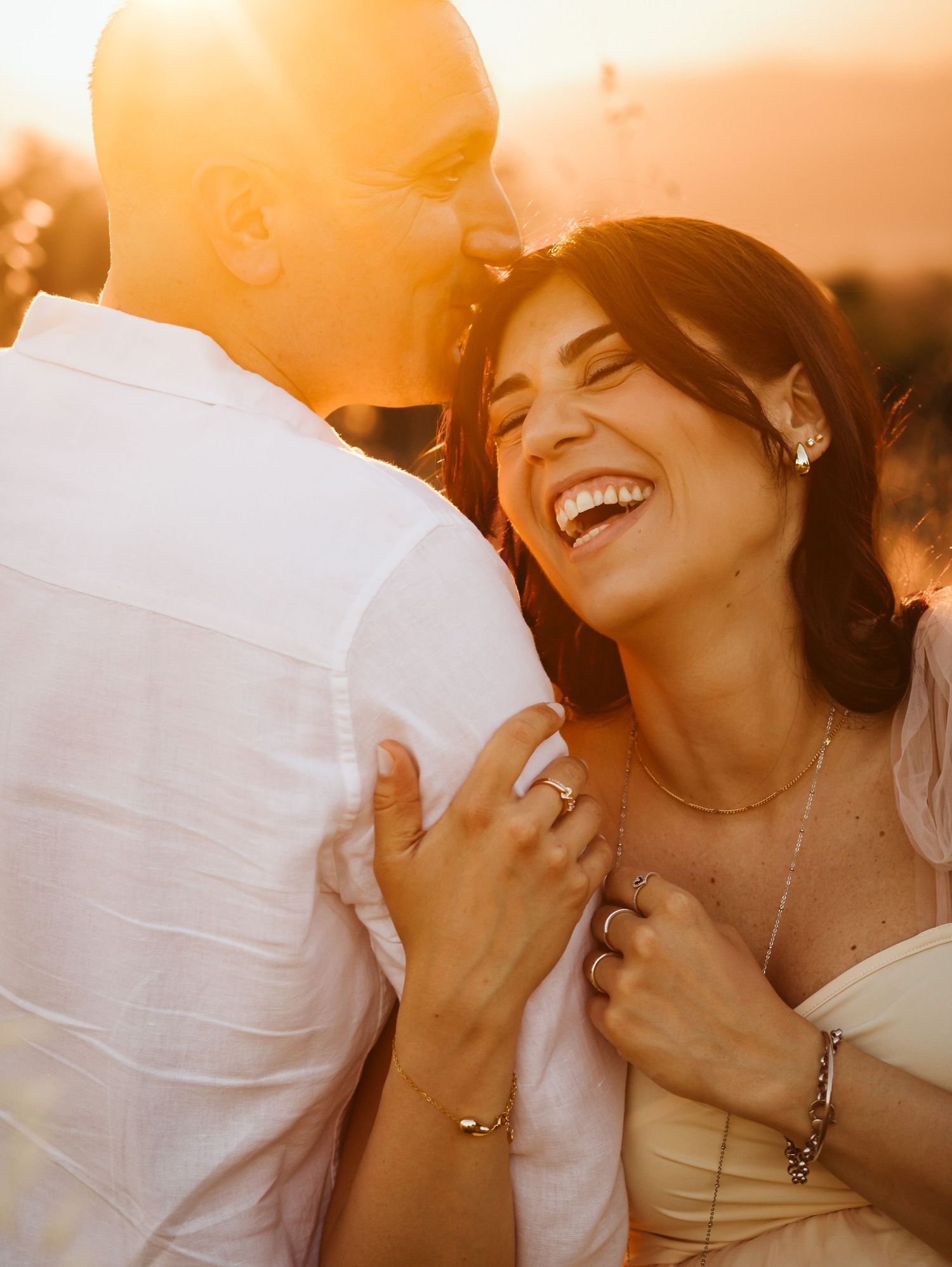 Joyful woman laughing in warm golden sunset light embraced by partner.