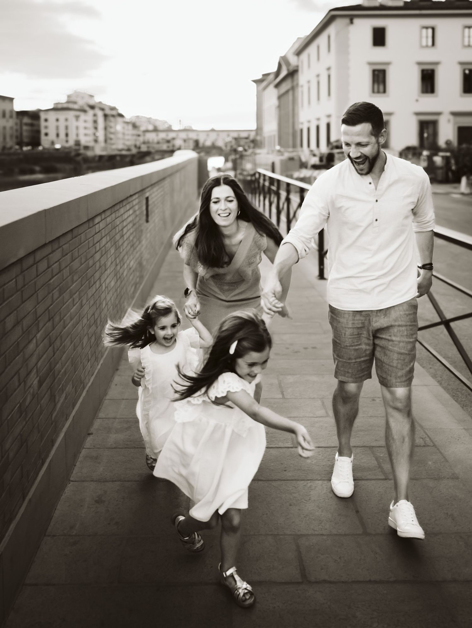 Black and white photo of energetic family running along a riverside walkway in Florence.