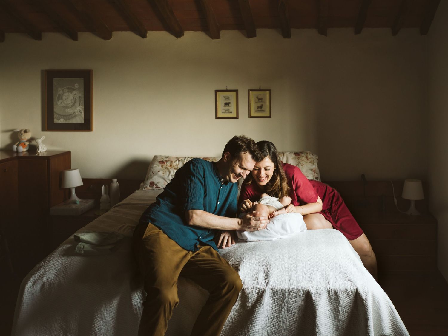 New parents lean over a bed to lovingly admire their newborn baby in a cozy rustic room.