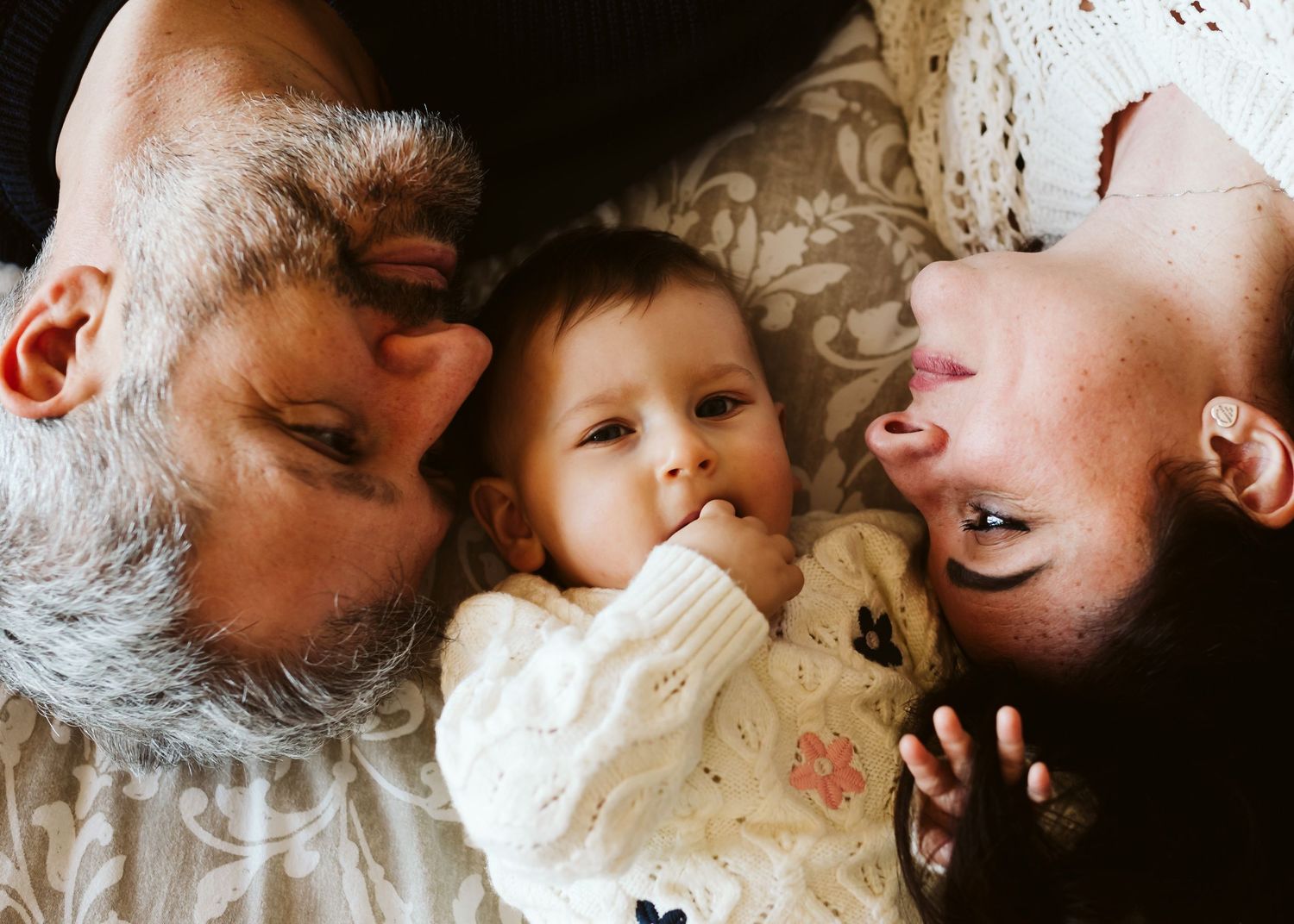 Overhead view of parents and baby lying together on floral bedding.