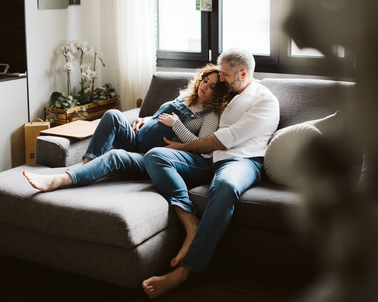 Pregnant couple relaxing together on a gray sofa in a cozy modern living room.