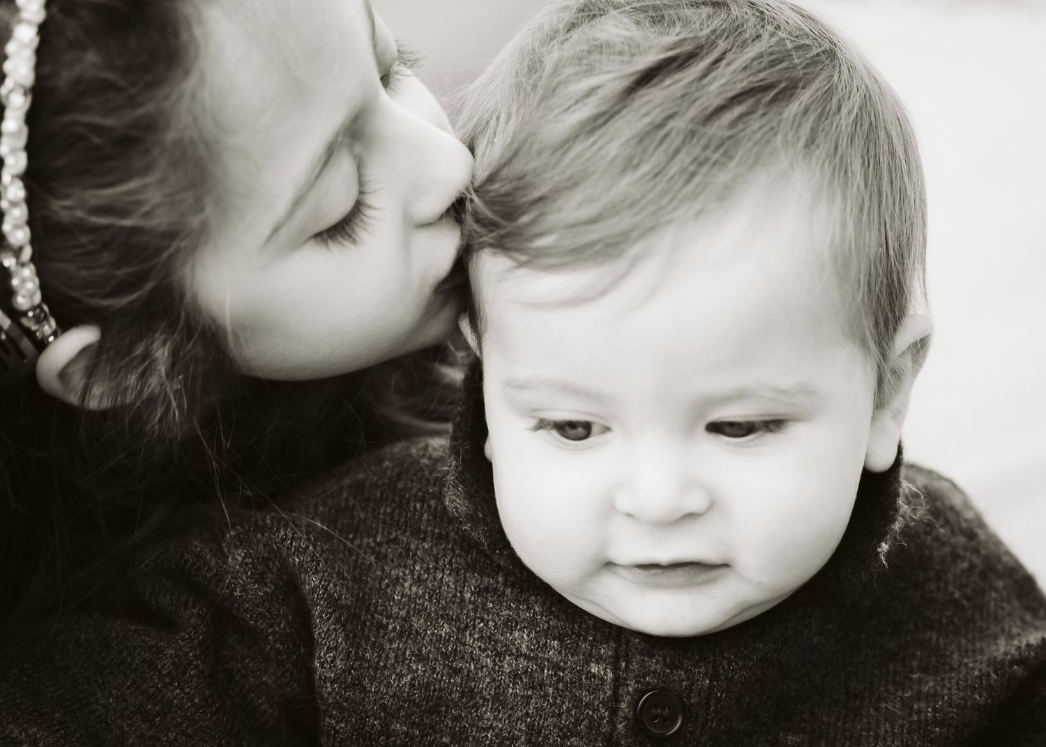 Black and white close-up of an older sibling gently kissing a baby on the head.