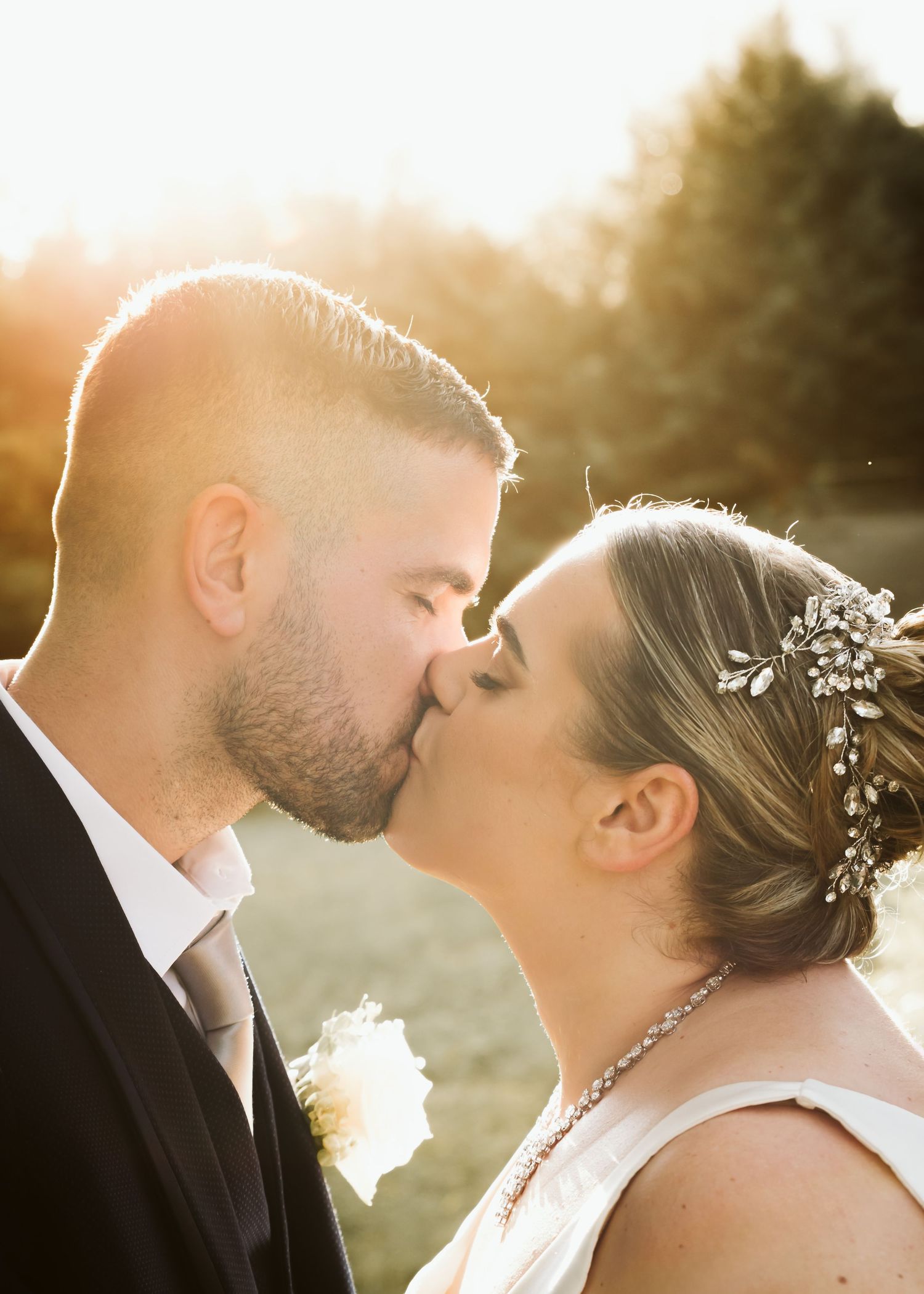 Bride and groom sharing a kiss in golden sunset light outdoors.