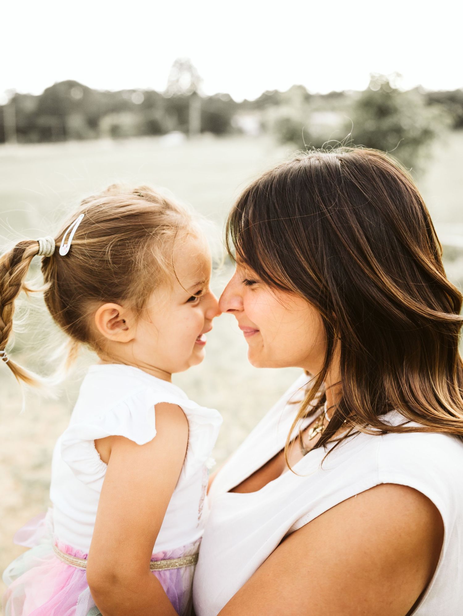 Mother and young daughter touching noses and smiling in sunny park.