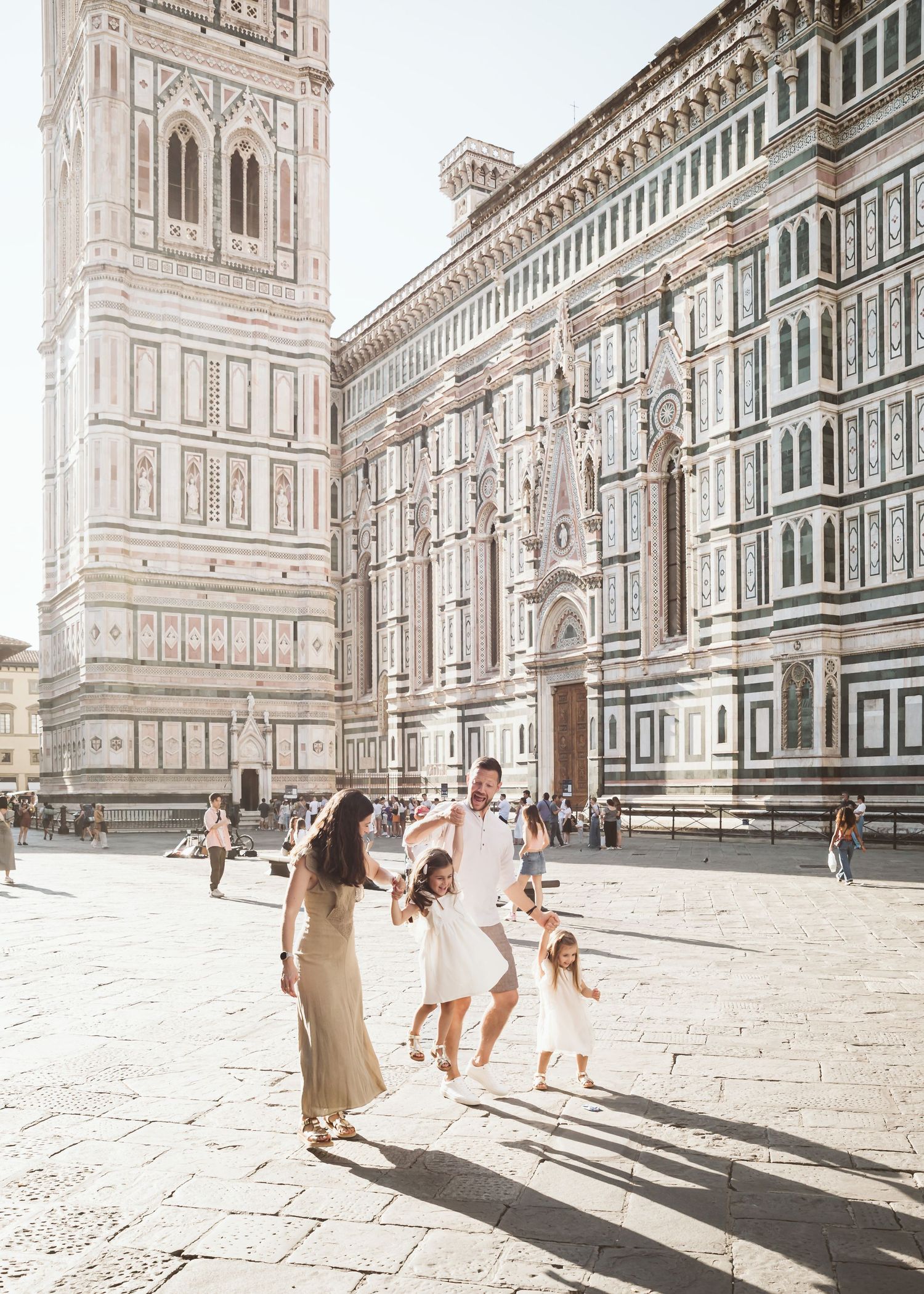 Happy family swinging children outside the Florence Cathedral on a sunny day in Italy.