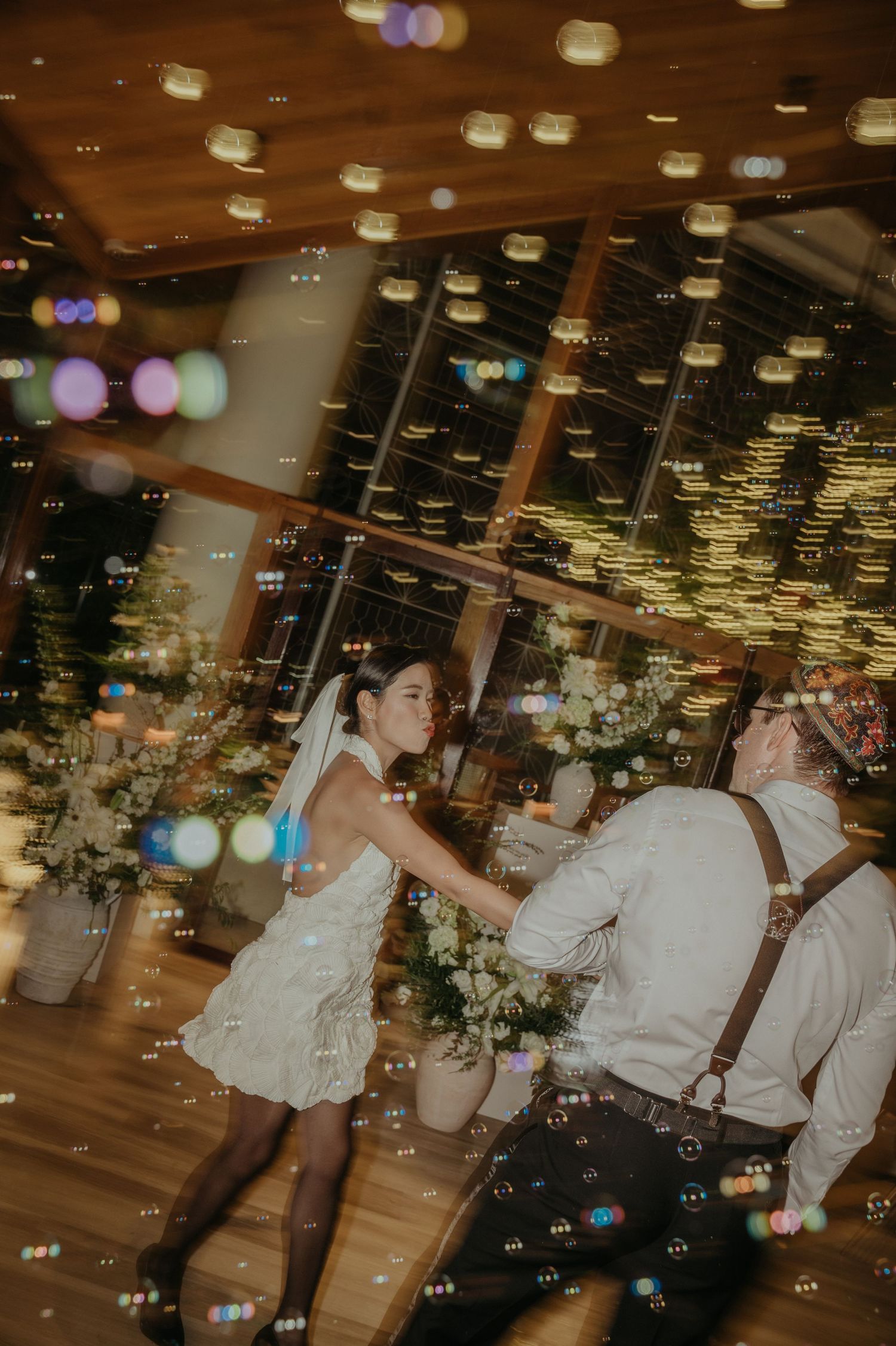 Newlyweds dancing energetically under bokeh lights at their reception.