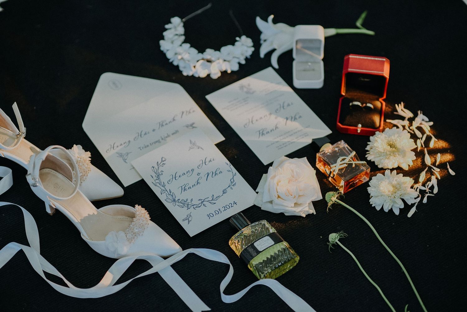 Wedding flat lay with invitation cards, flowers, ribbons and accessories on dark background.