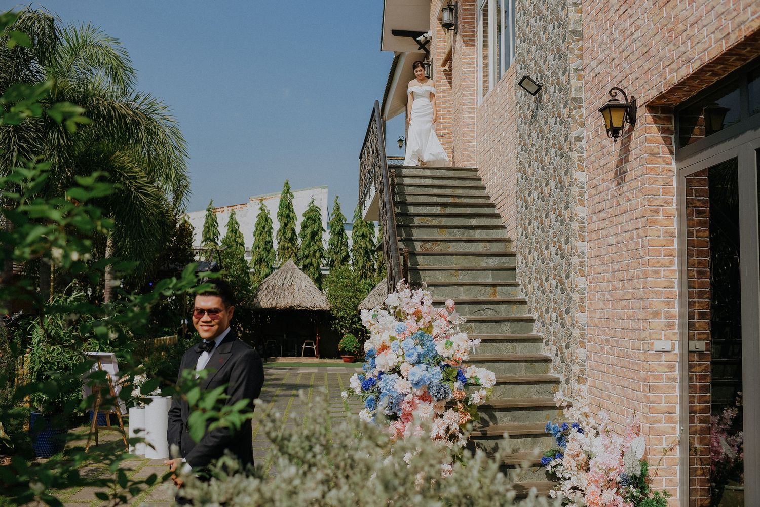 Wedding couple poses on ornate brick staircase decorated with pastel flowers and greenery.