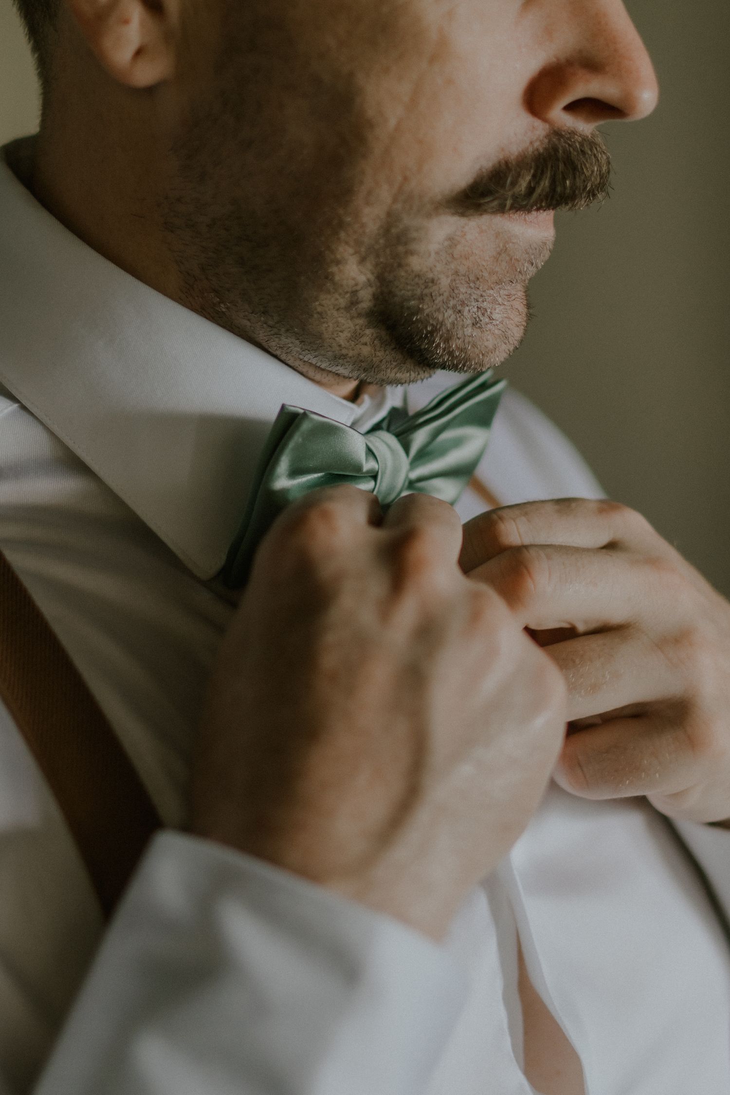 Close-up detail of a sage green bowtie being adjusted on a white dress shirt collar.