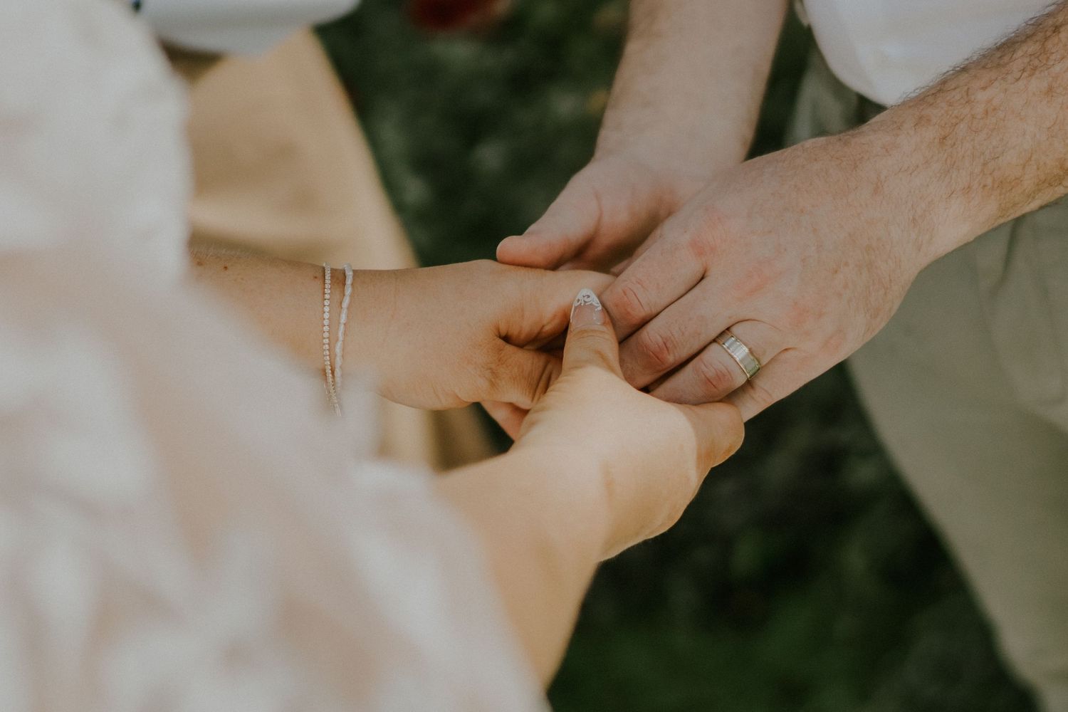 Close-up of hands joining together during outdoor wedding ceremony.