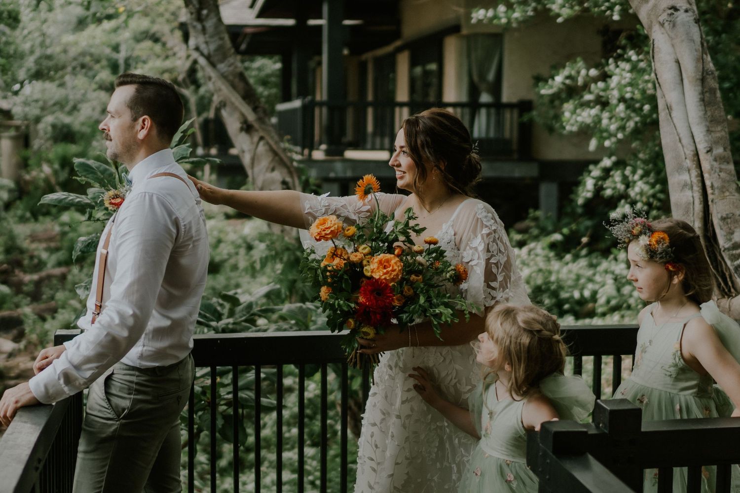 A playful wedding party moment captured on a wooden balcony surrounded by lush trees.