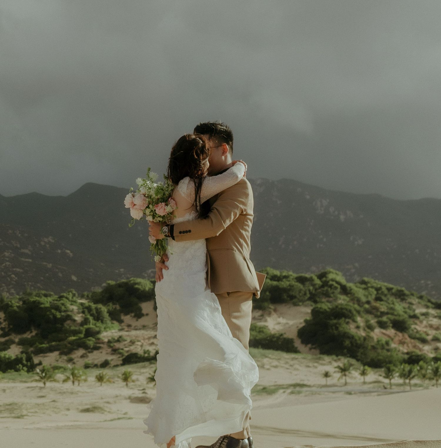 A couple shares an intimate moment against a scenic mountain backdrop during a desert wedding ceremony.