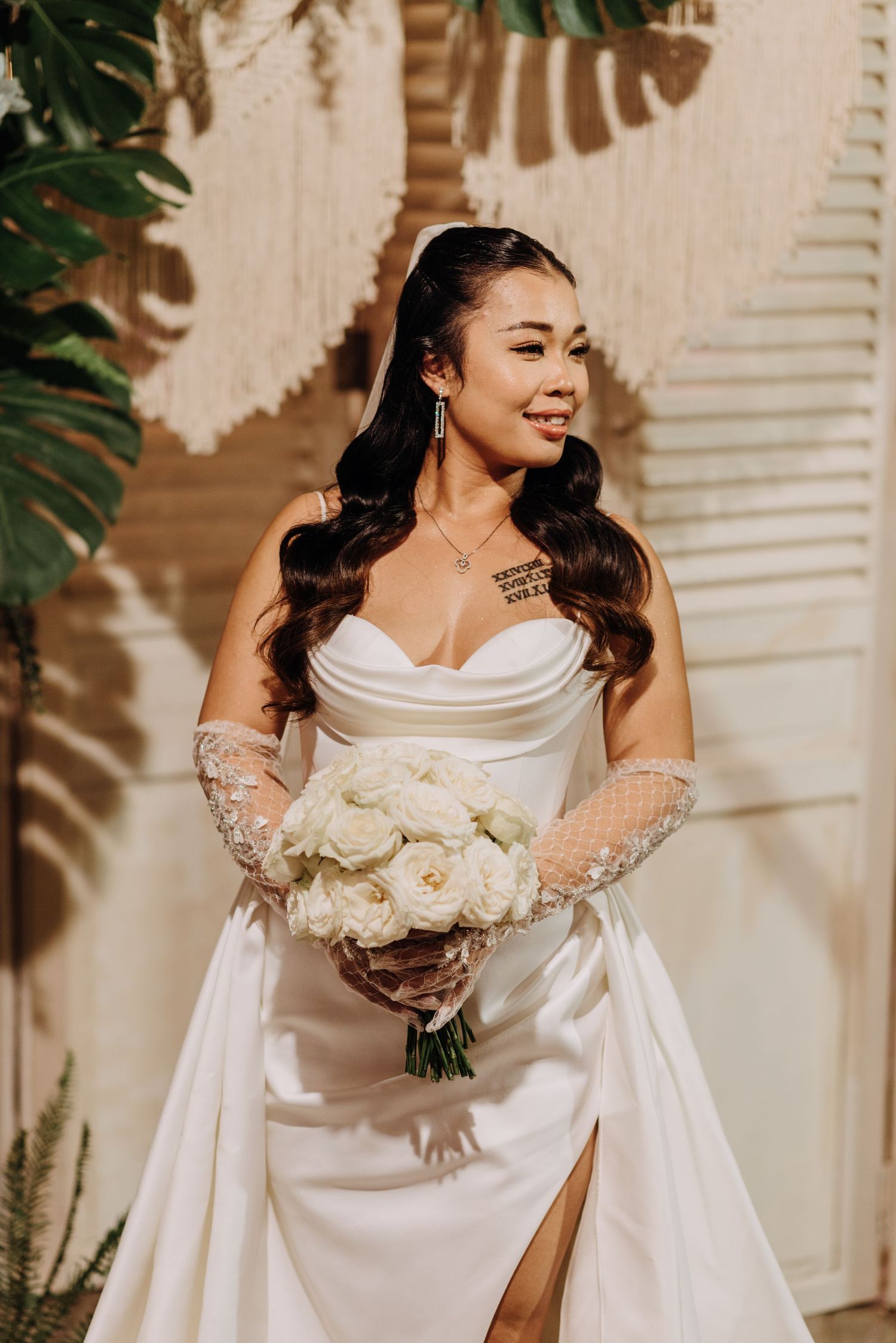 A bride in a white satin dress with a thigh slit holds a bouquet of white roses.