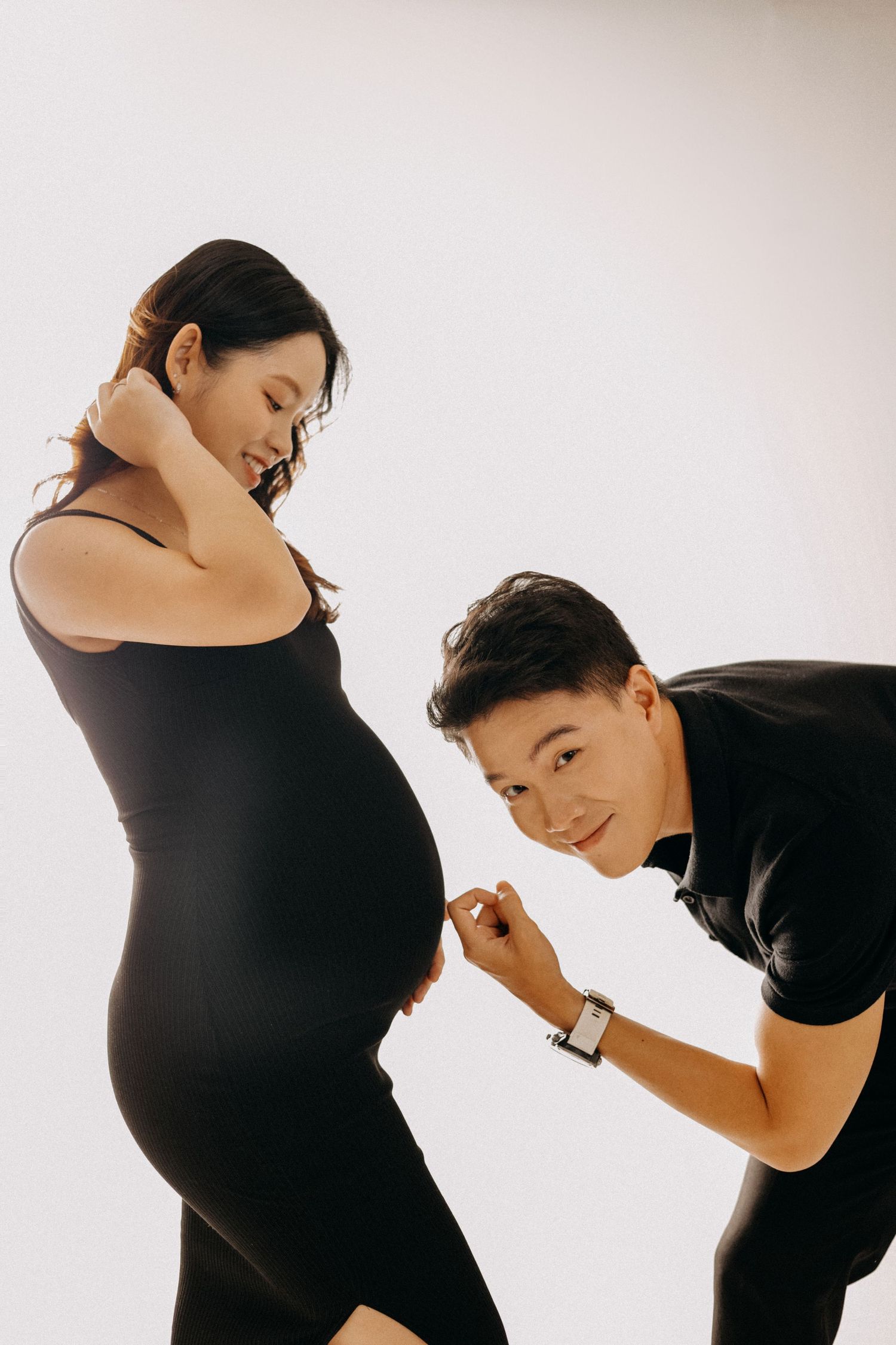 A playful maternity photo with couple in black outfits against white background.