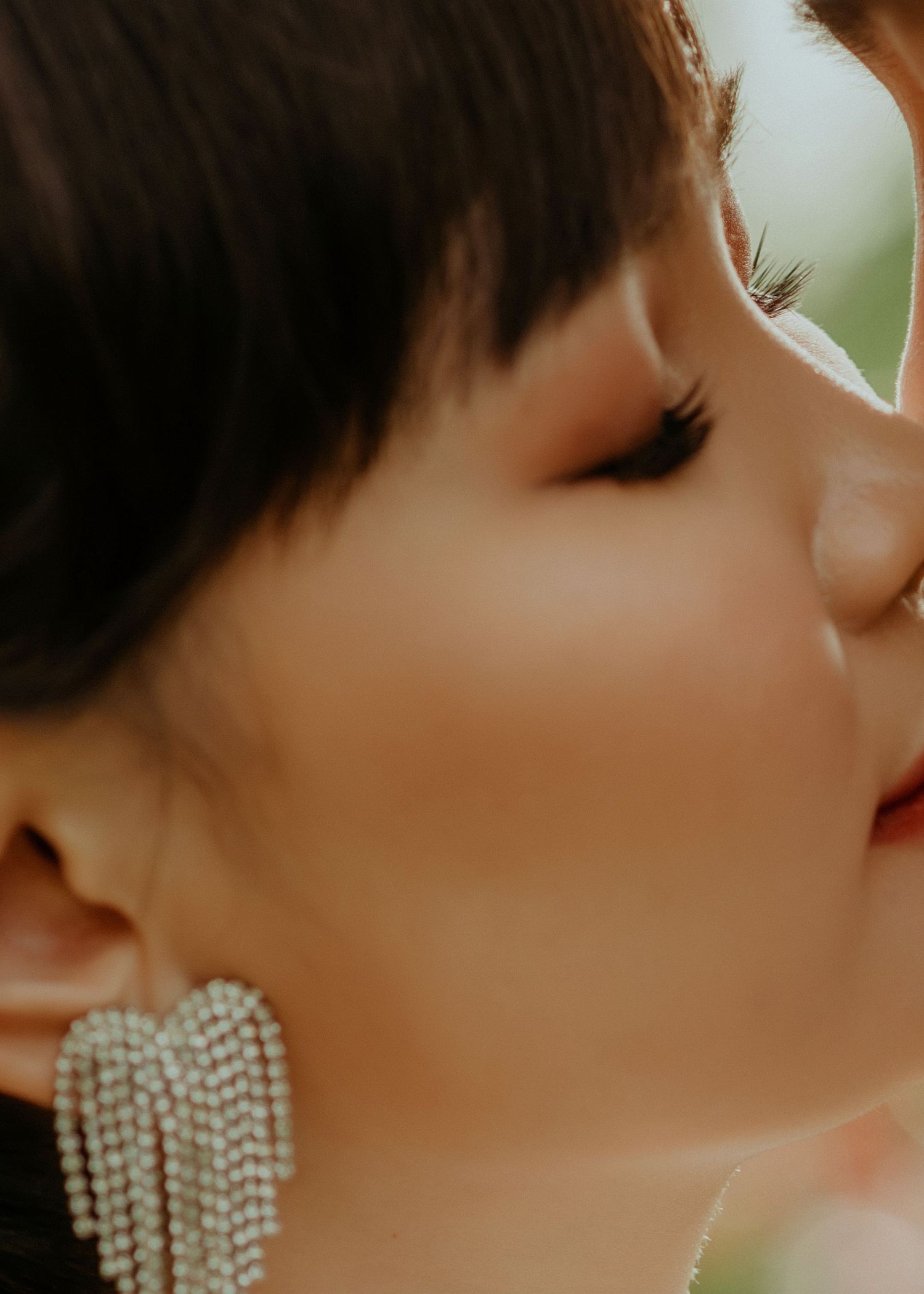 Close up profile view of a person wearing sparkly heart-shaped dangle earrings in warm lighting.