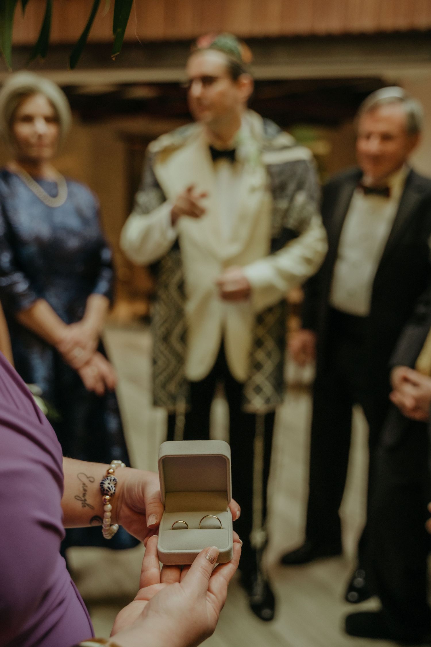 A close-up of hands holding an open ring box during a formal event.