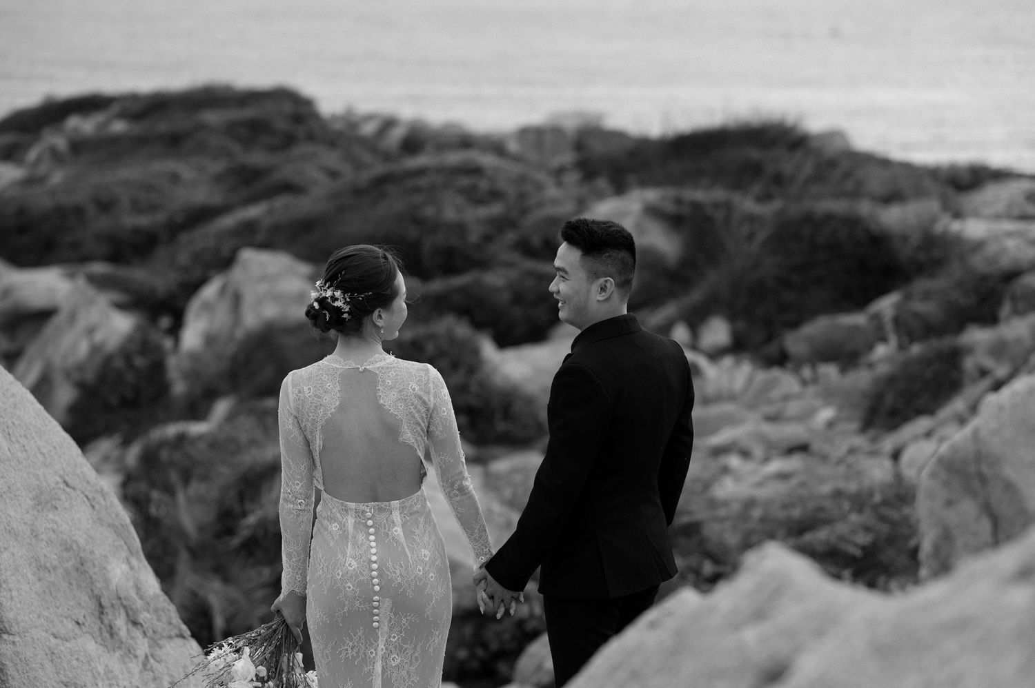 A couple holding hands while standing together in a rocky mountainous landscape in black and white.
