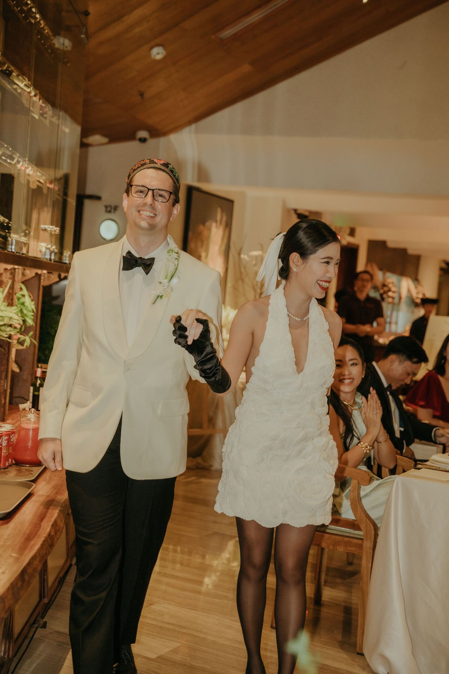 Newlyweds walk through their reception venue in formal attire.