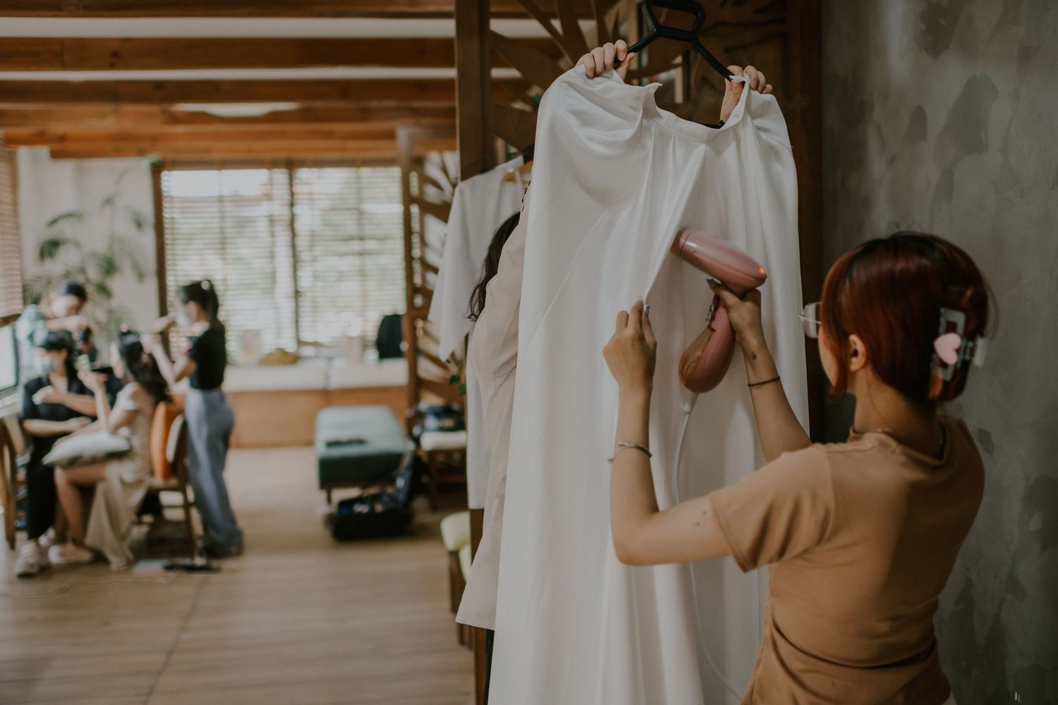 Person arranging white wedding dresses on hangers in preparation room.