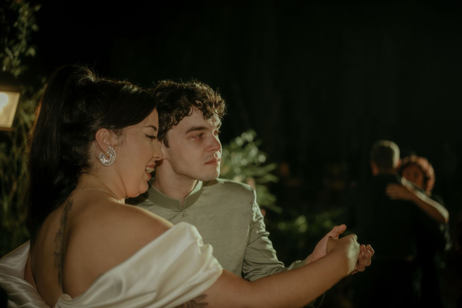 A couple dances together at an evening wedding reception in a romantic, dimly lit outdoor setting.