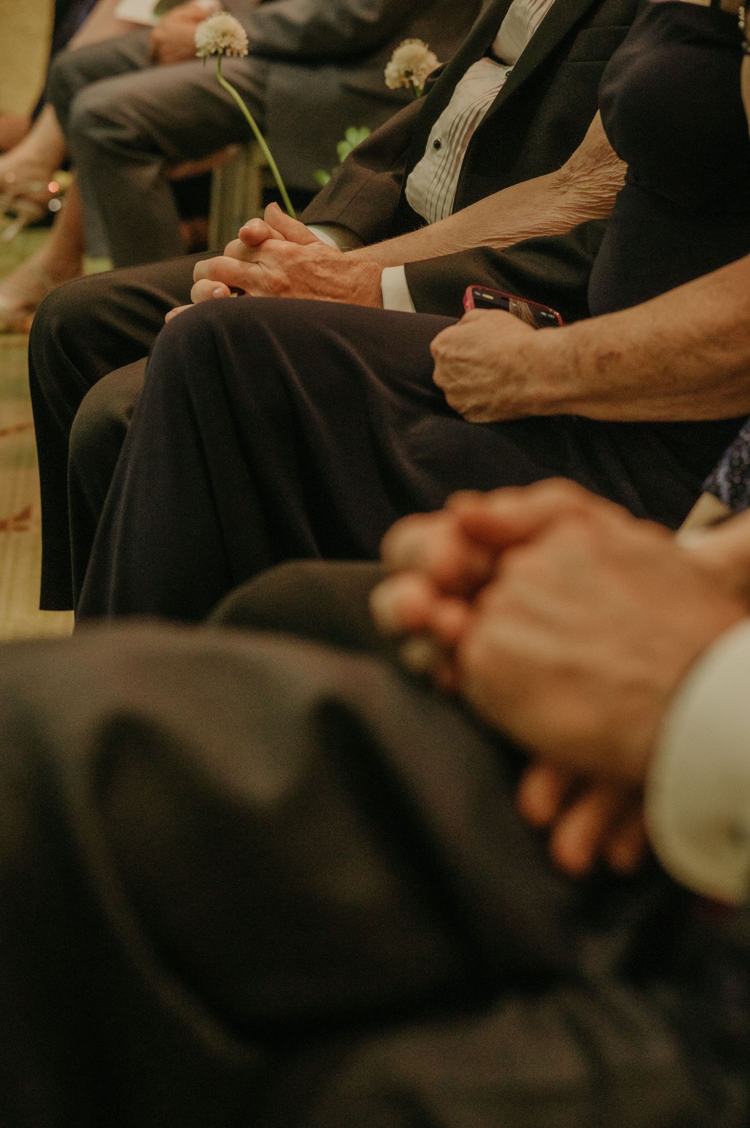 Detail shot of wedding guests' hands clasped together during the ceremony.