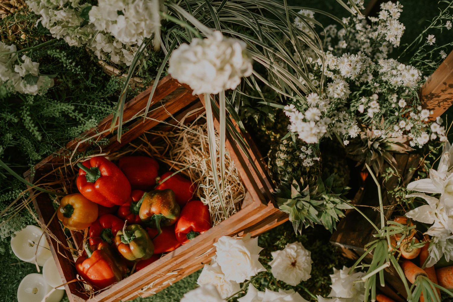 Fresh red bell peppers nestled in a wooden crate surrounded by delicate white flowers and greenery.