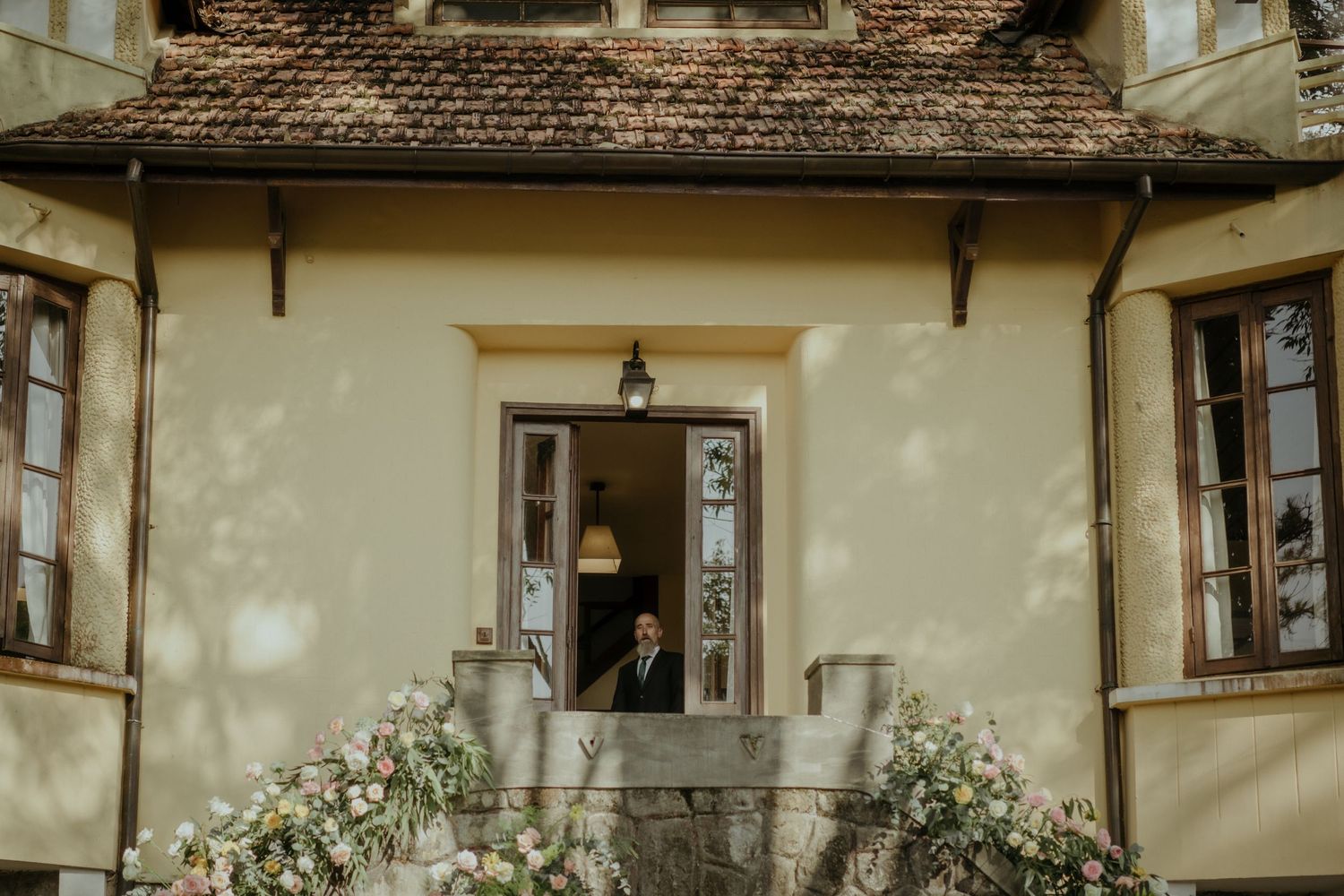A charming rustic cottage entrance with cream colored walls and climbing white roses around vintage windows.