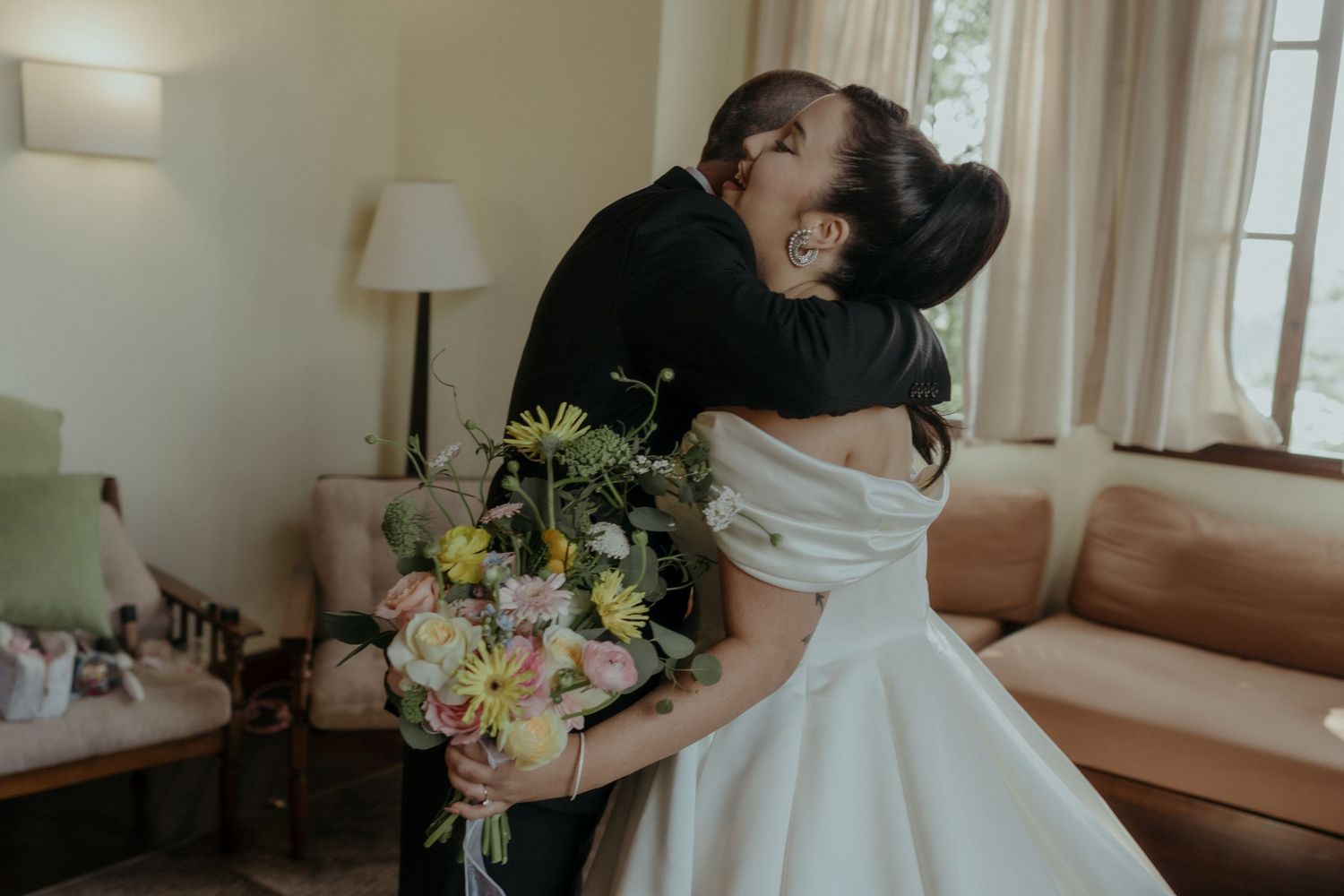 Two people share an intimate moment in an elegant room with a beautiful floral bouquet and natural window lighting.