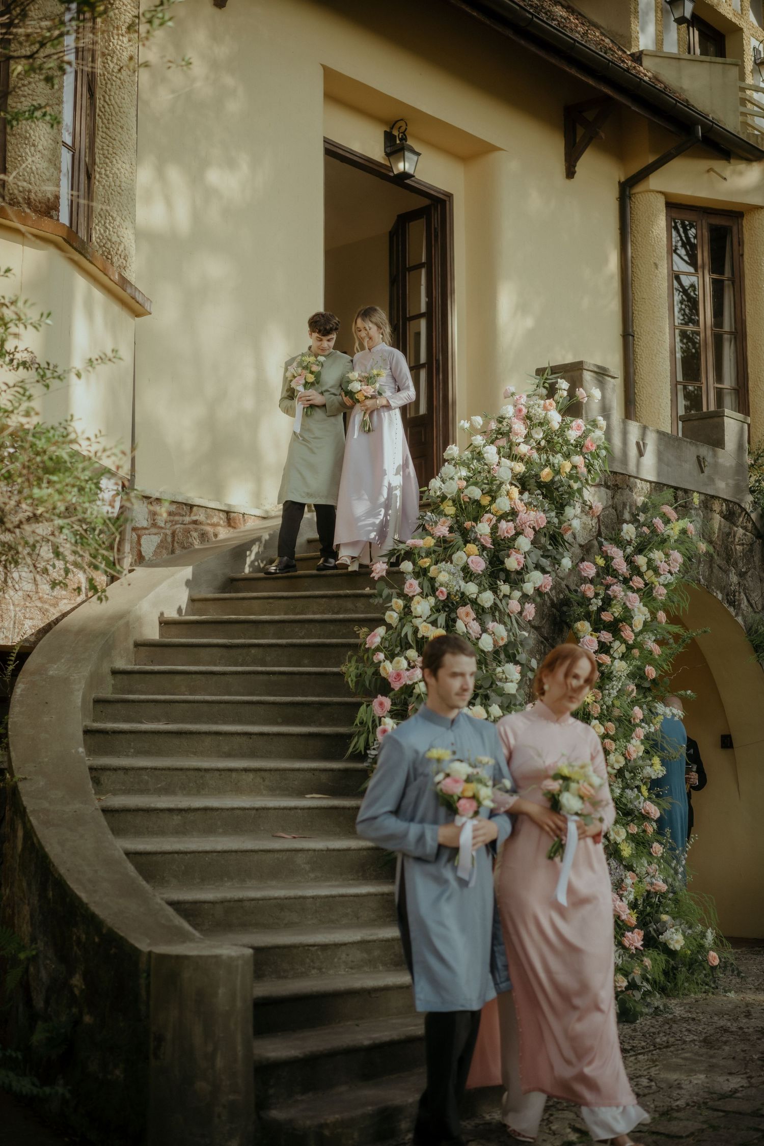 A vintage-style scene on curved stone steps with floral decorations and people in elegant period attire.