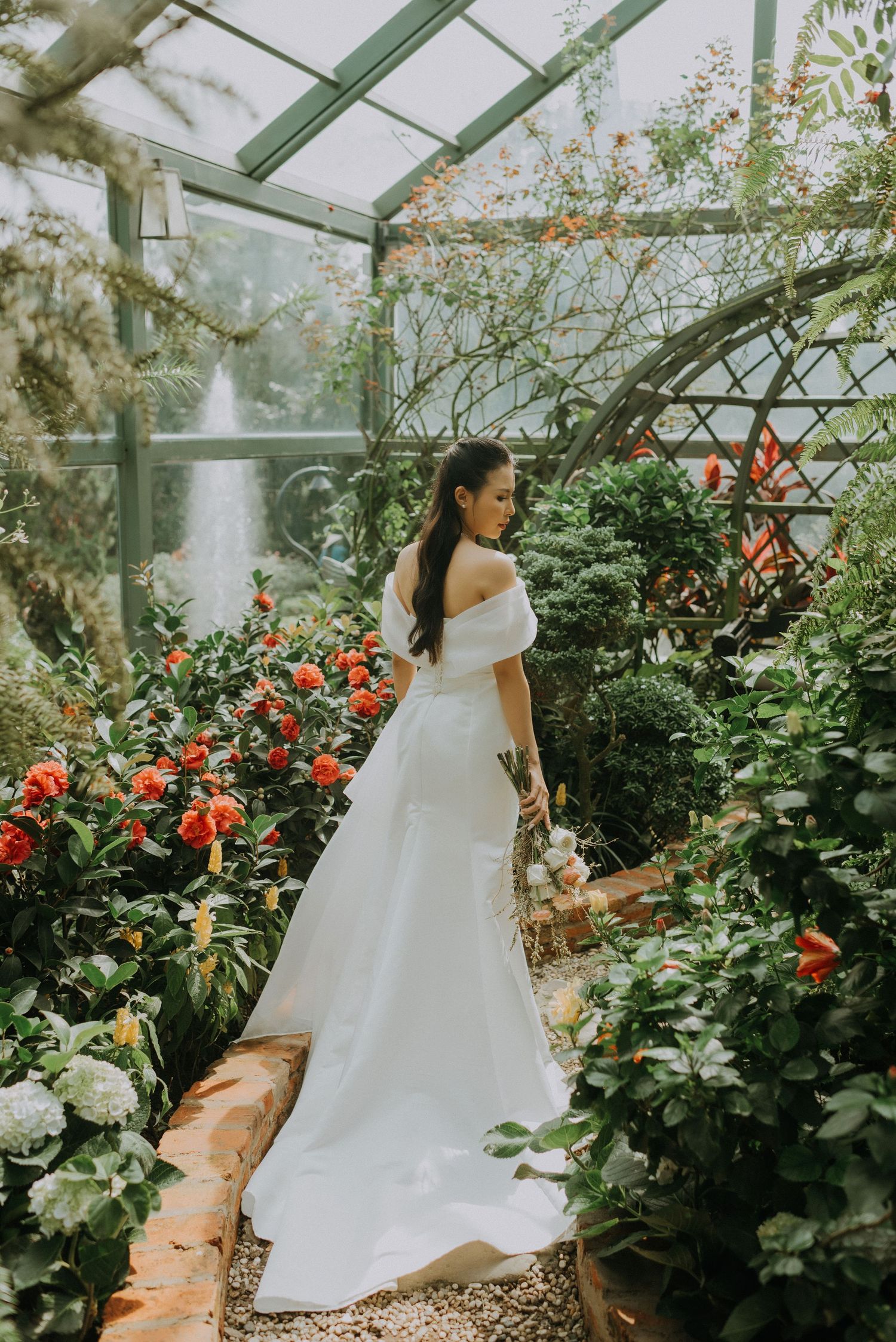 A dreamy greenhouse scene with a flowing white dress among blooming red roses and lush greenery in soft natural light.