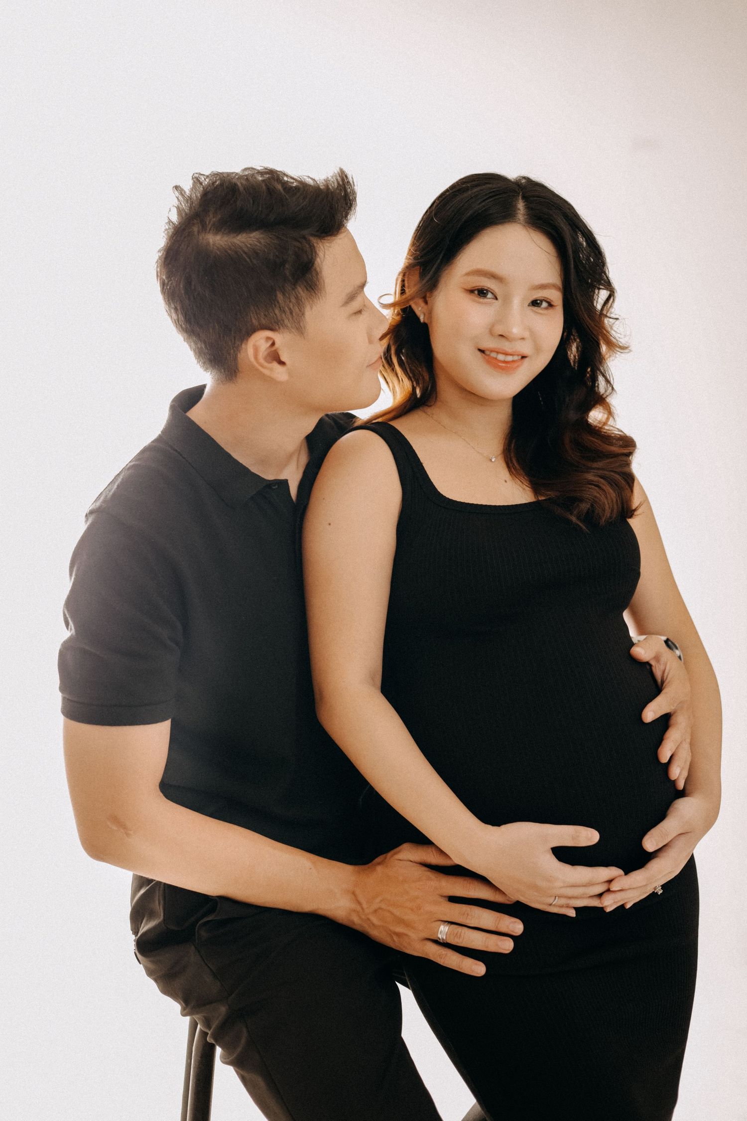 A couple shares an intimate moment during their maternity photoshoot against a white backdrop.