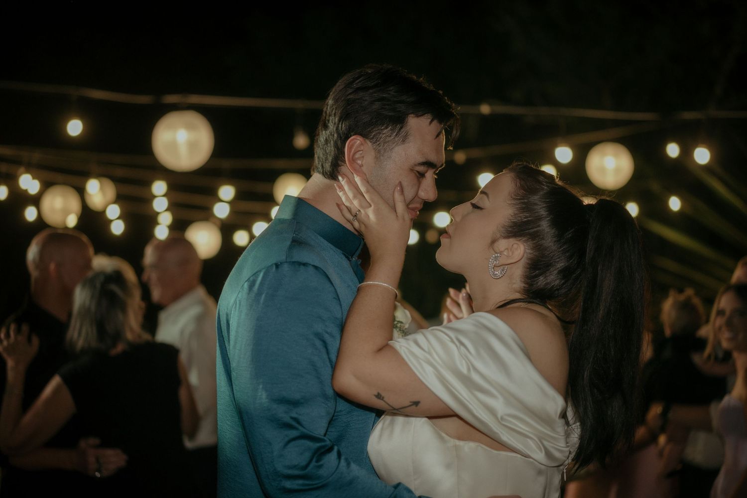 A couple embraces and dances intimately under glowing lanterns at a dimly lit evening reception.