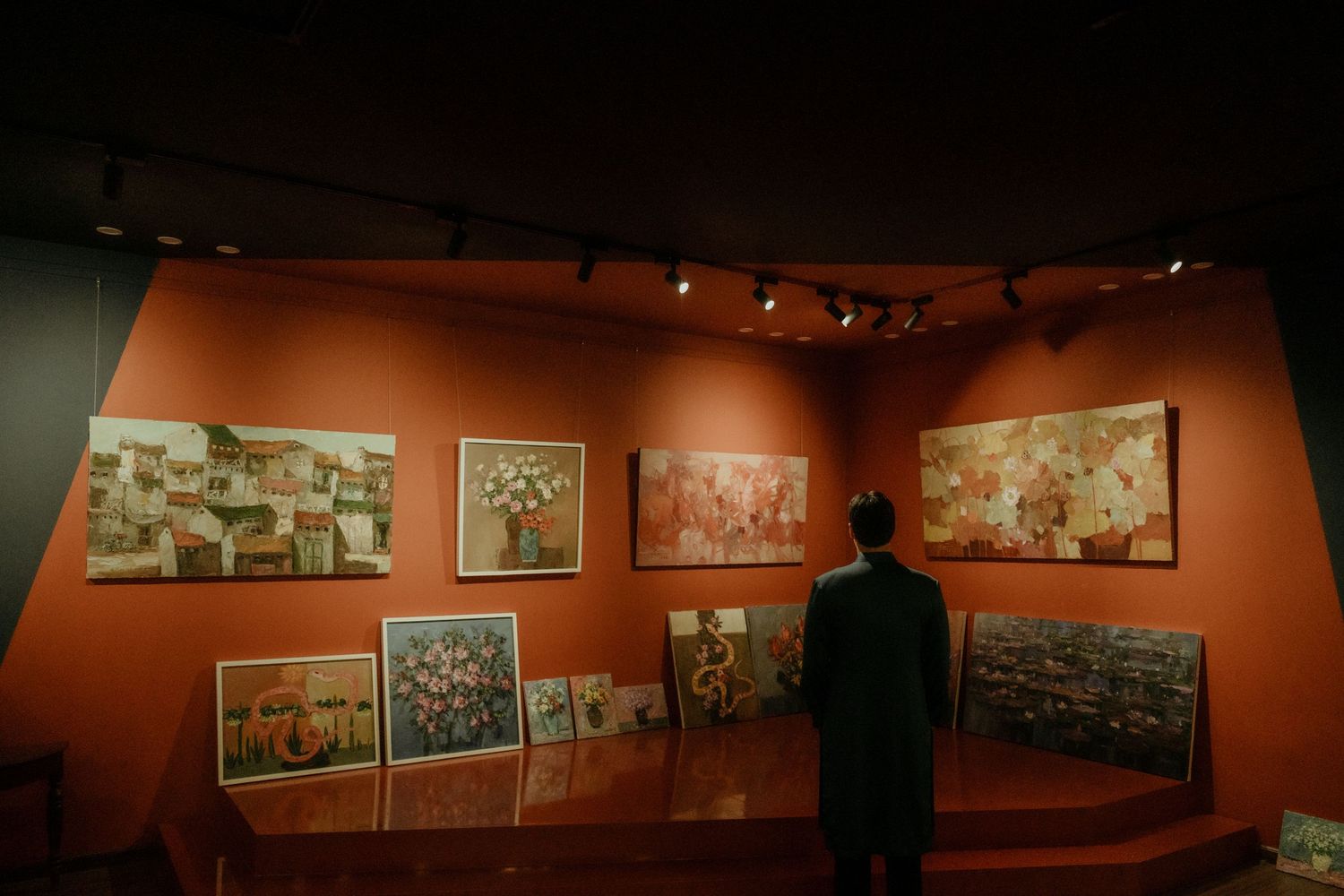 A person views vintage photographs displayed on an orange wall in a dimly lit museum exhibition space.