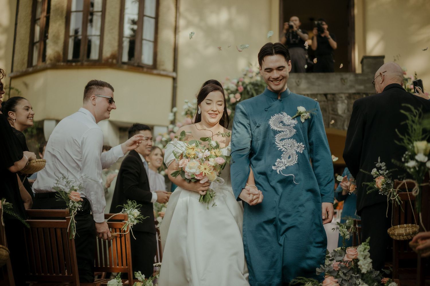 Joyful couple walking down the aisle at wedding ceremony with colorful floral decorations and teal attire.
