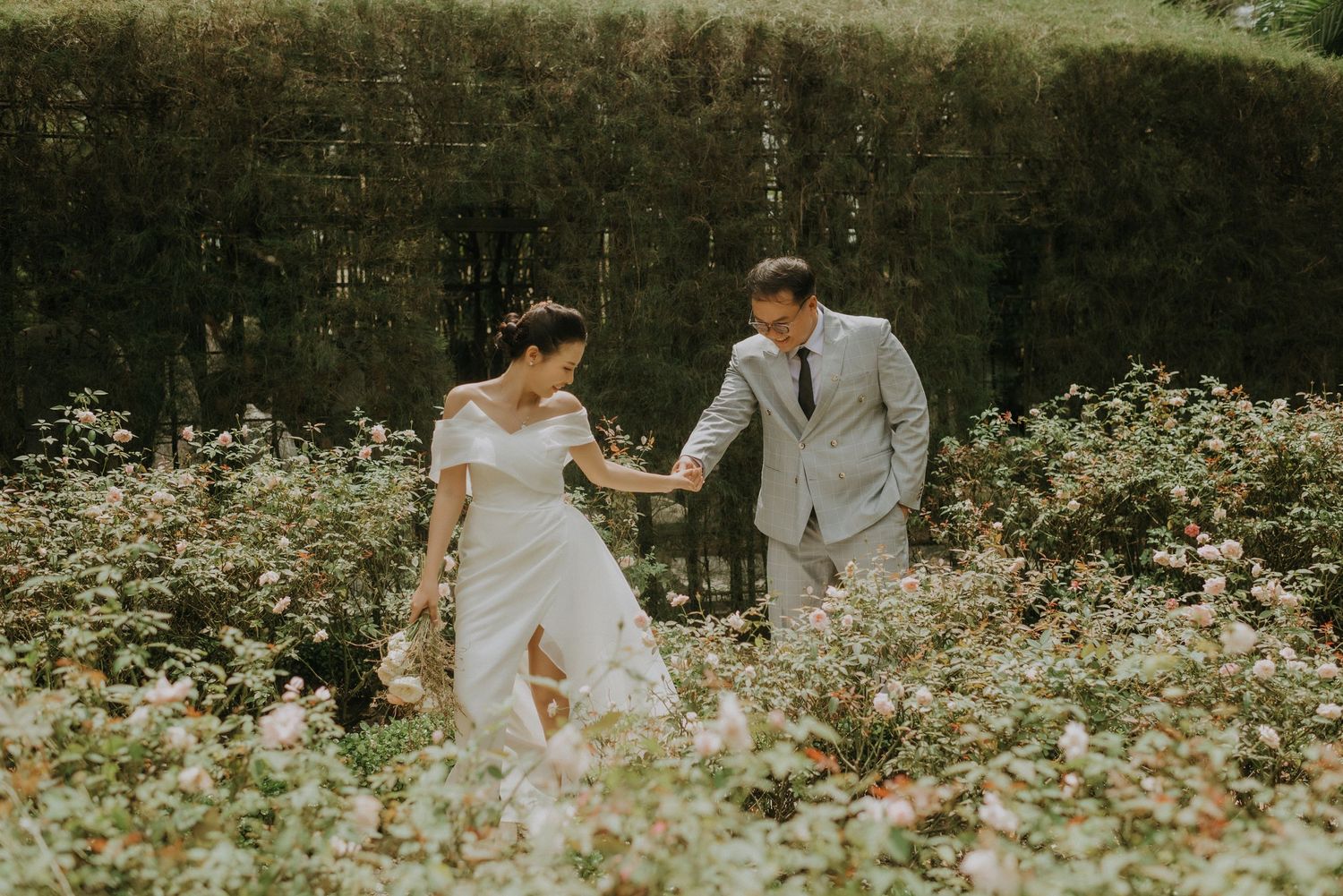 A couple in wedding attire walk hand in hand through a dreamy wildflower meadow on their special day.