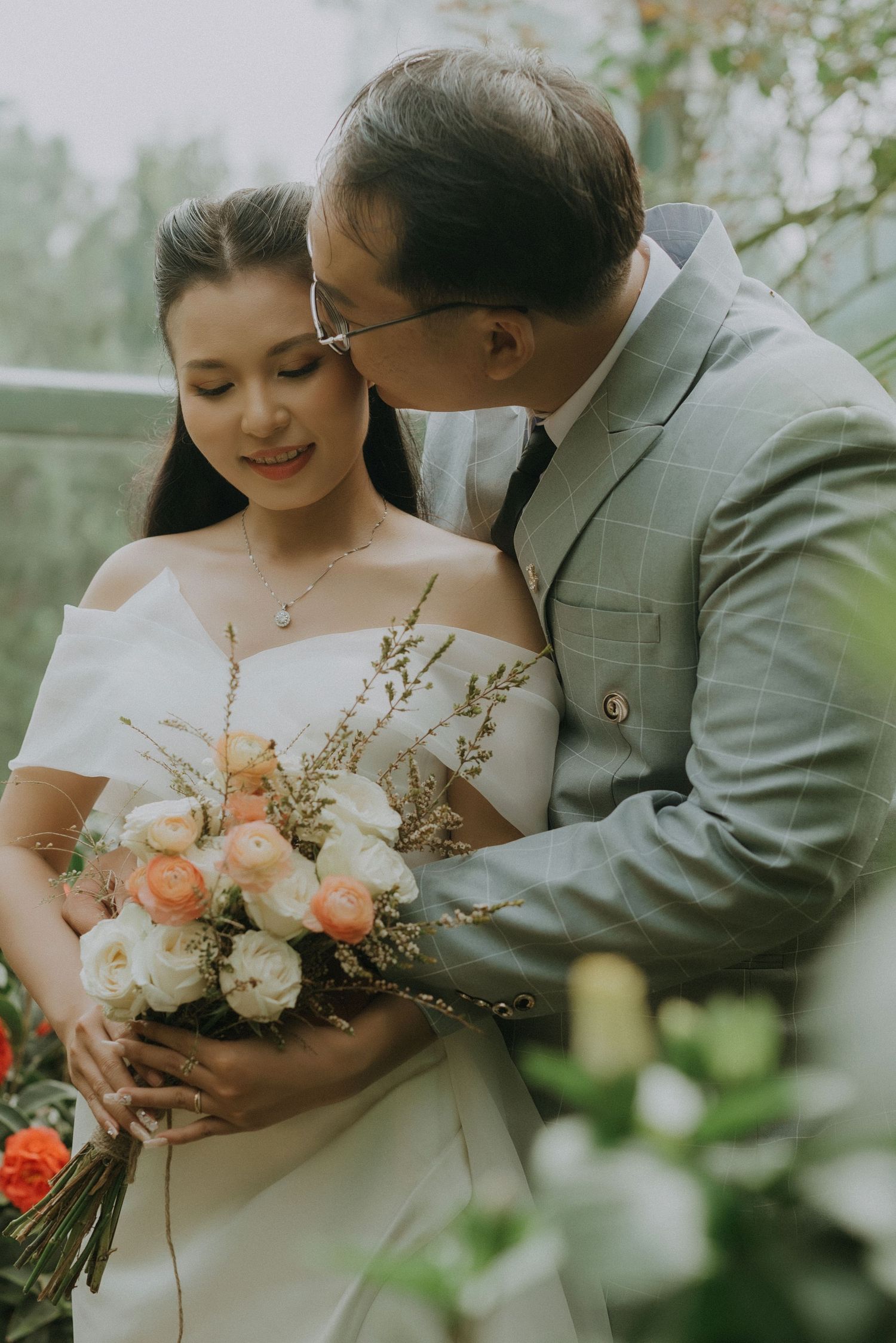 A romantic wedding moment captured outdoors with a beautiful bouquet of peach and white roses against a dreamy natural backdrop.
