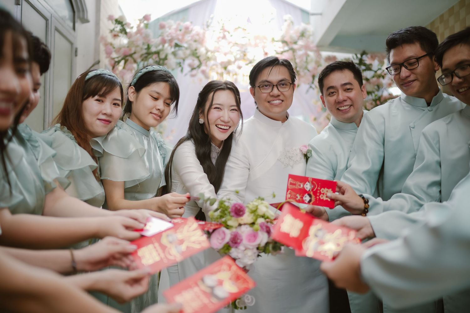 Wedding party gathered in a circle exchanging red gift envelopes during celebration.