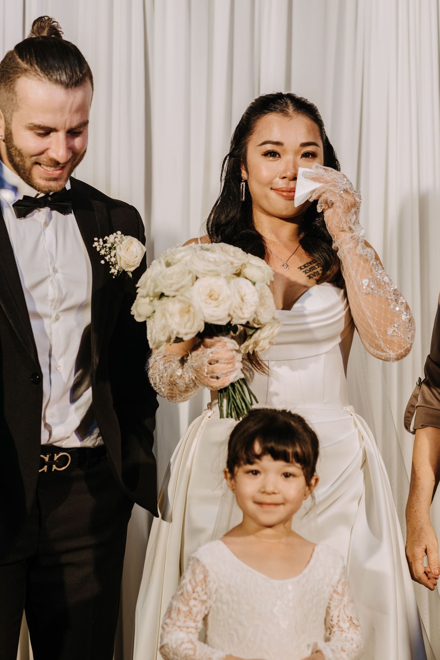 A wedding party poses together with the flower girl in white lace dress.