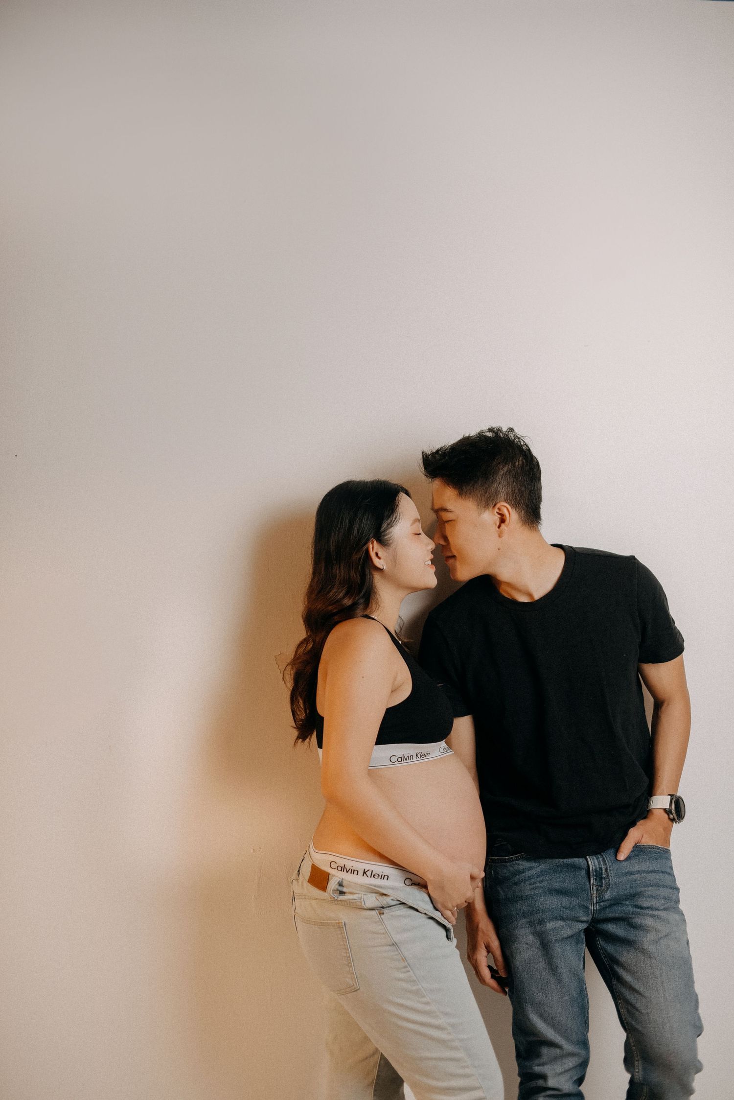 An intimate maternity photo of a couple against a plain wall.