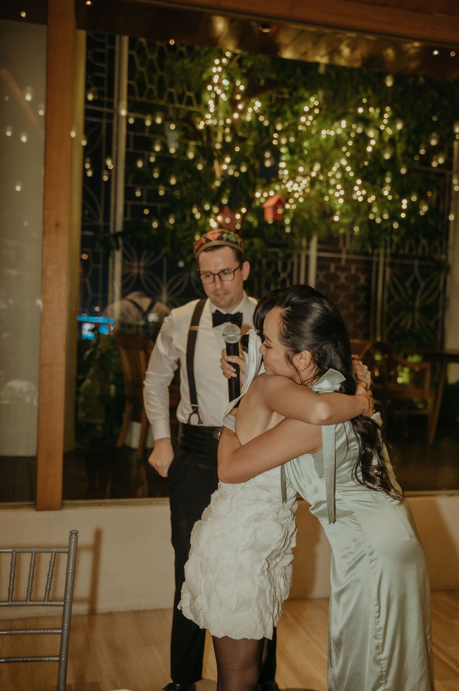 Emotional moment during wedding reception with twinkle lights and greenery backdrop.