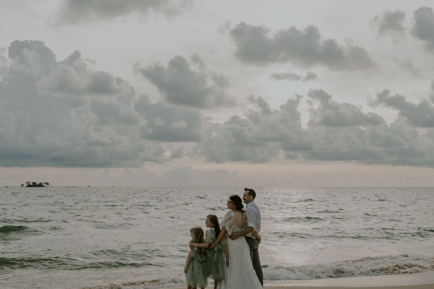 Silhouetted family watches sunset over ocean during beach wedding celebration.