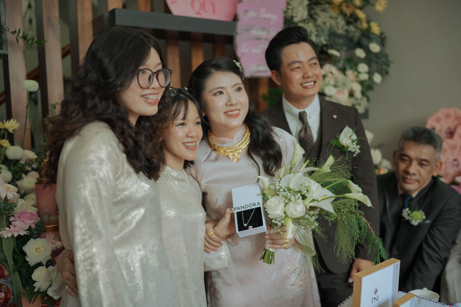 Wedding party members pose together during Vietnamese celebration with floral decorations.
