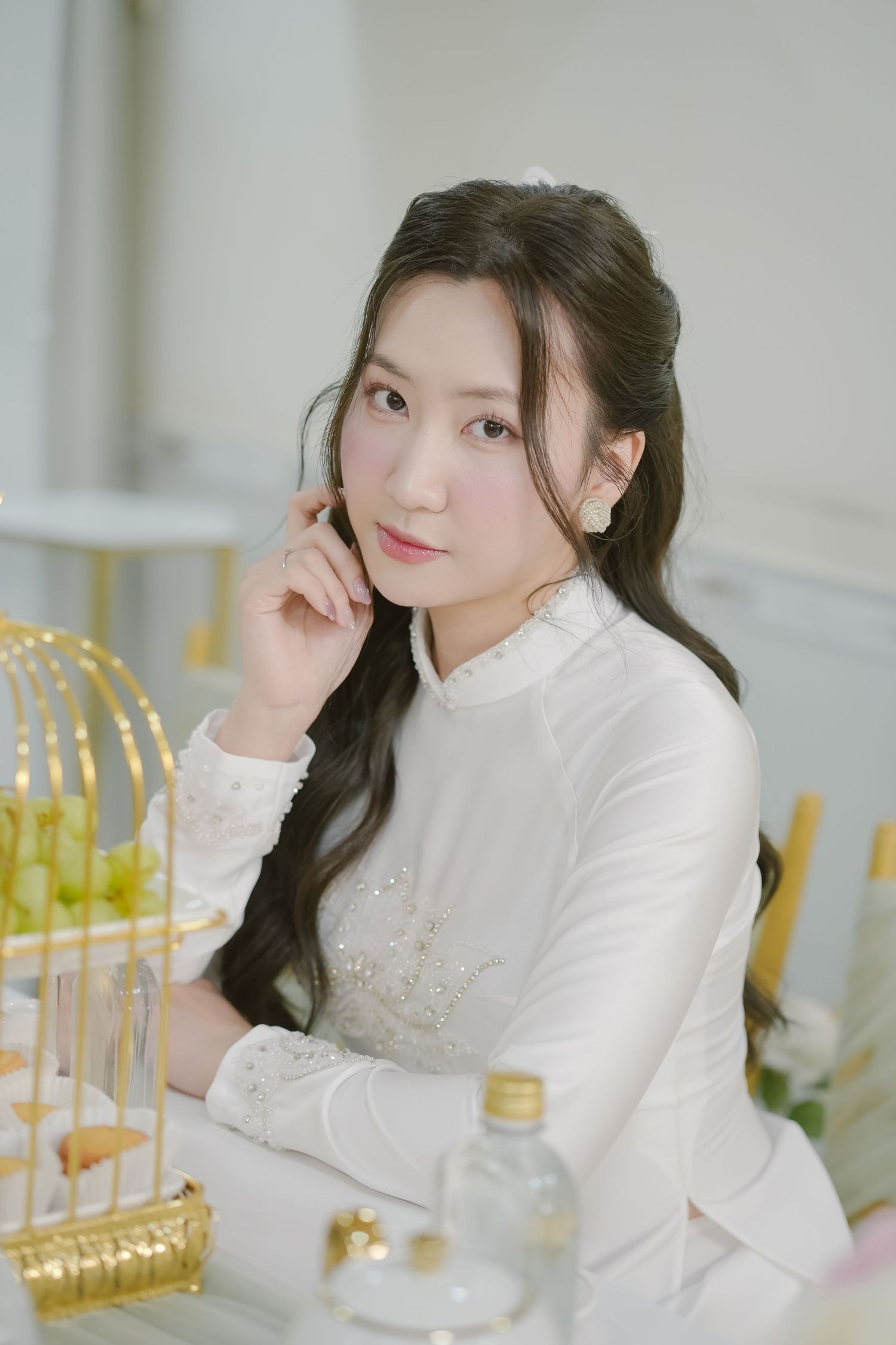 Elegant white ao dai dress shown with decorative gold birdcage and floral decor.